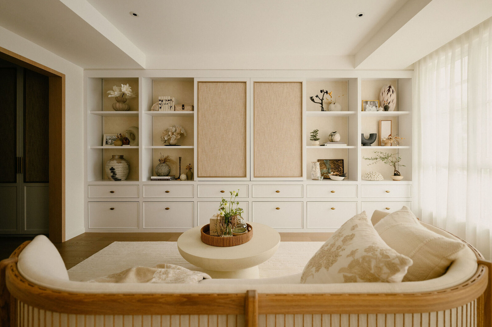 Living area with bespoke built-in shelving, curated decorative objects, and a curved sofa in soft neutral tones.