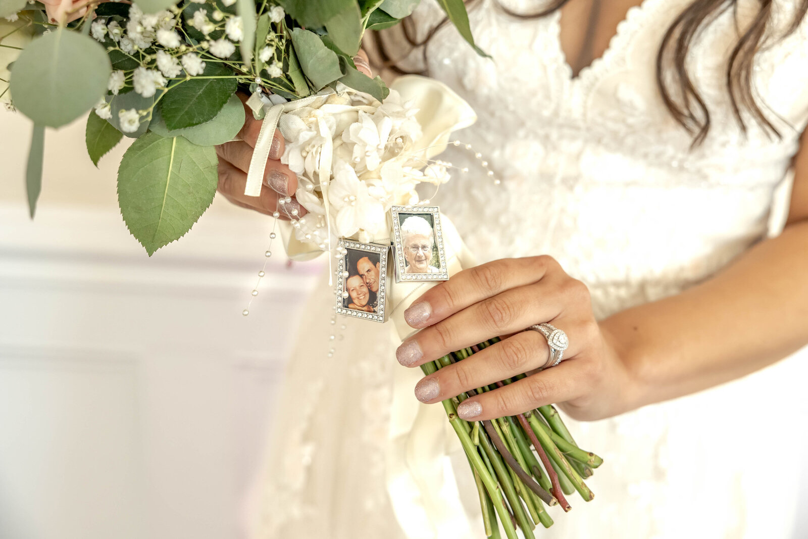 The bride holds a bouquet adorned with memorial photo charms, featuring greenery and white florals, captured during a Wilmington, NC wedding, showcasing thoughtful and sentimental wedding details.