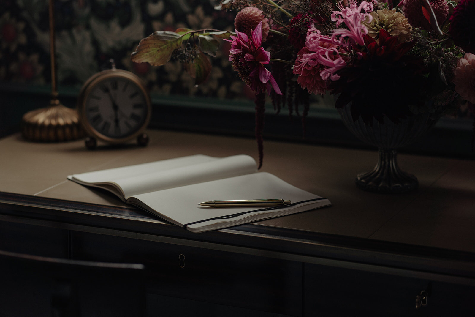 ©Ethos_Imagery - Moody image of a note book on a desk next to a floral arrangement created by Fleuris Orchard & Blooms at Rosemead House in Esquimalt, Victoria, BC. 