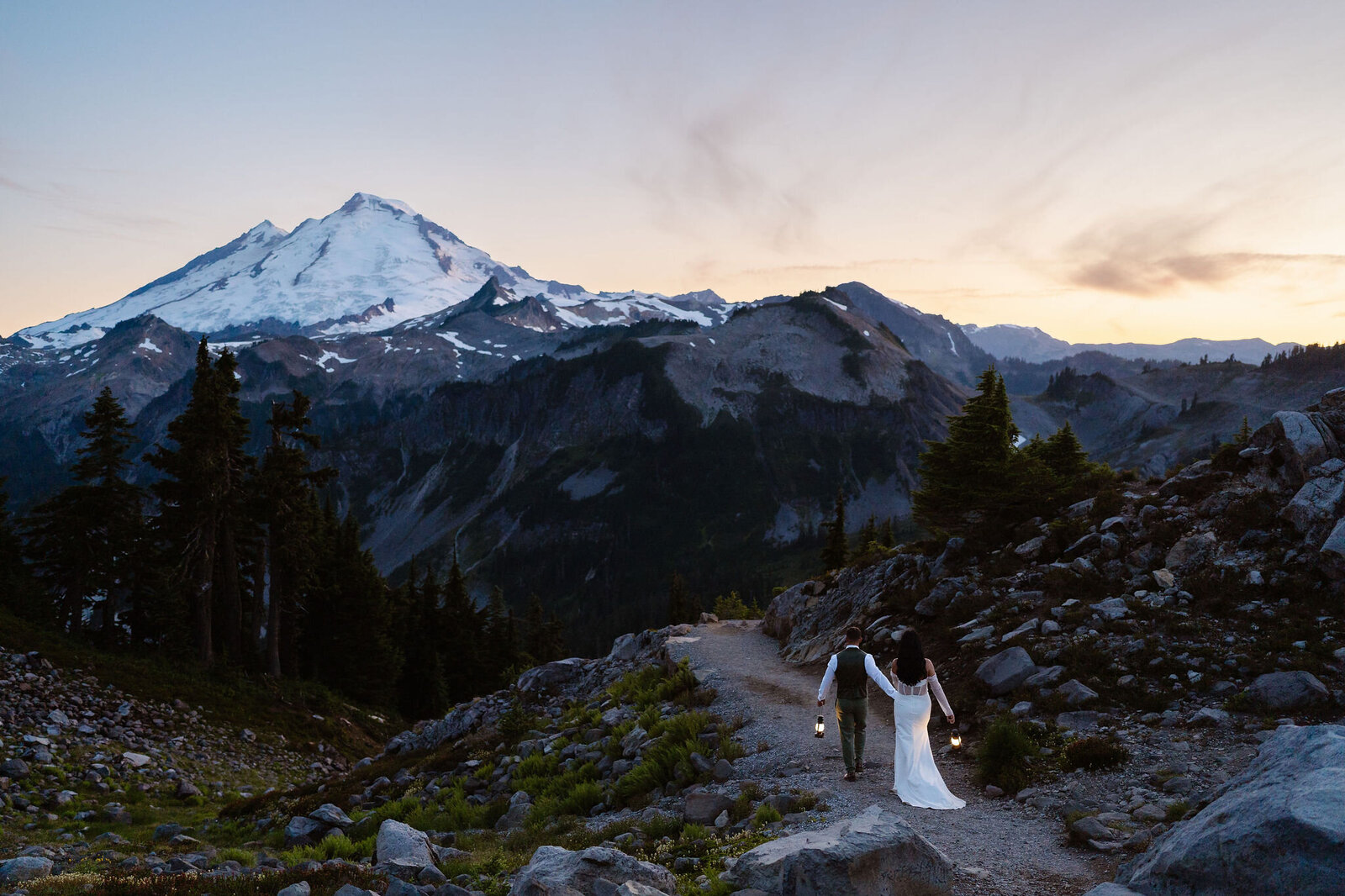a couple holds hands and lanterns as they walk off into the sunset towards Mount Baker during their Washington elopement