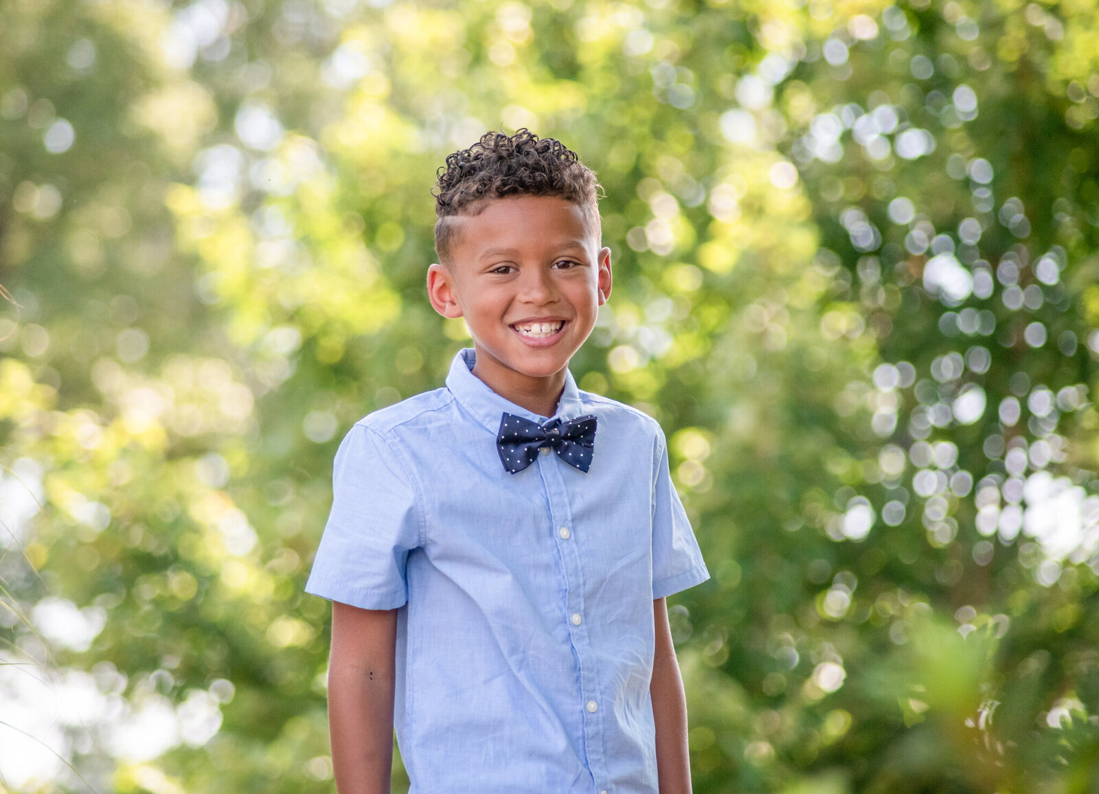 young boy in a blue dress shirt with a blue bow tie standing outdoors photographed by Millz Photography in Greenville, SC
