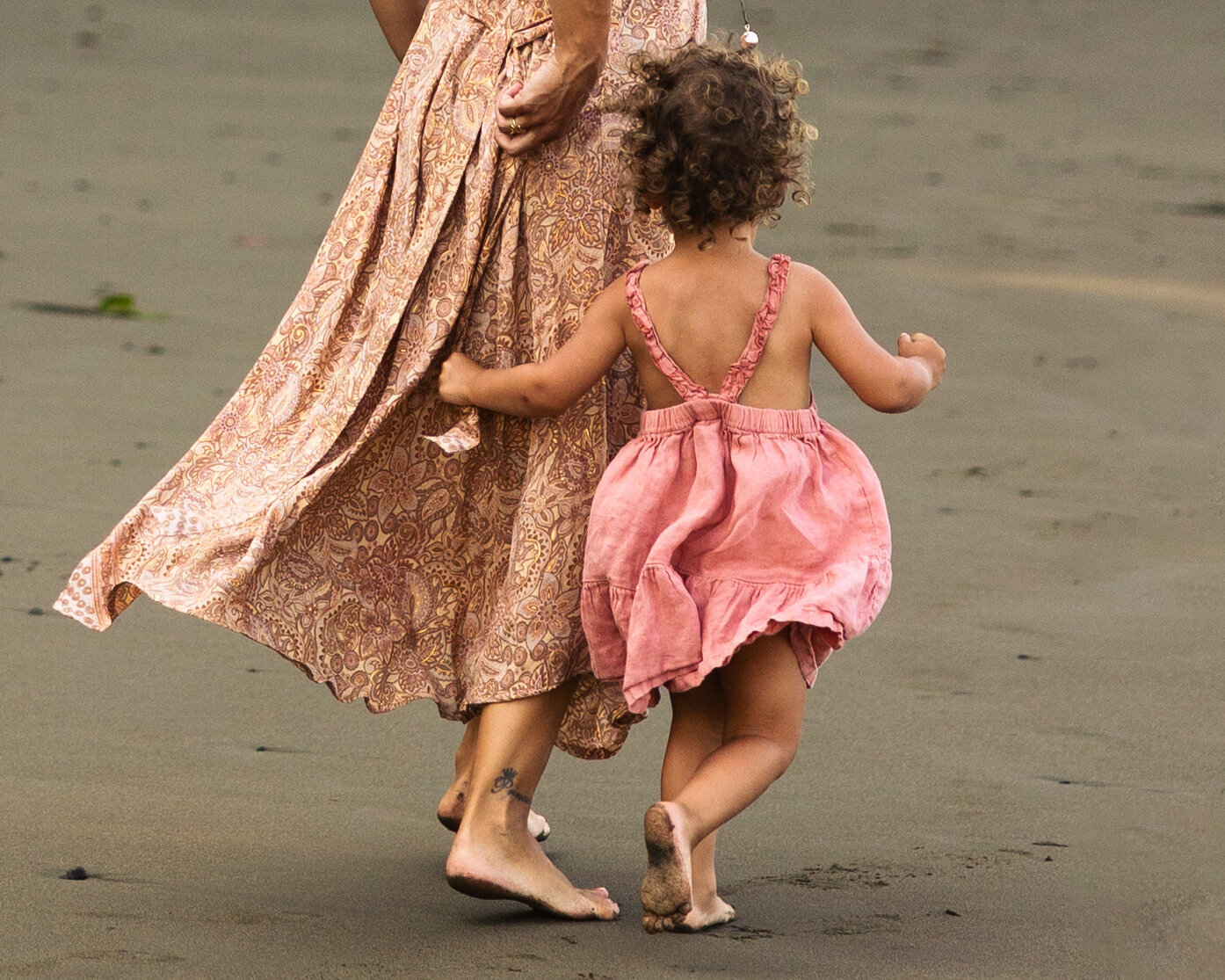 Toddler girl chasing mother on the beach with pink flowy dresses