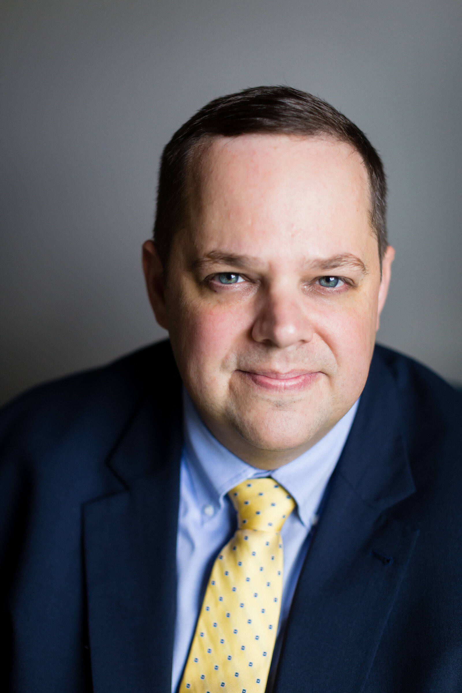 man wearing navy blue suit smiling for camera with yellow tie
