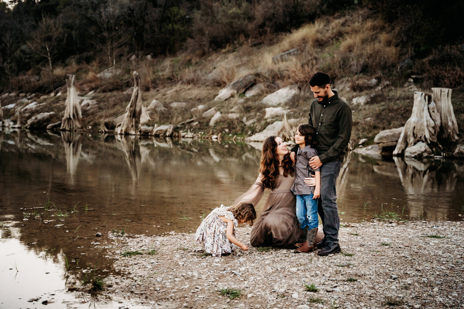 Maternity Photographer, a young family of 4 stands near quiet river, mom is pregnant