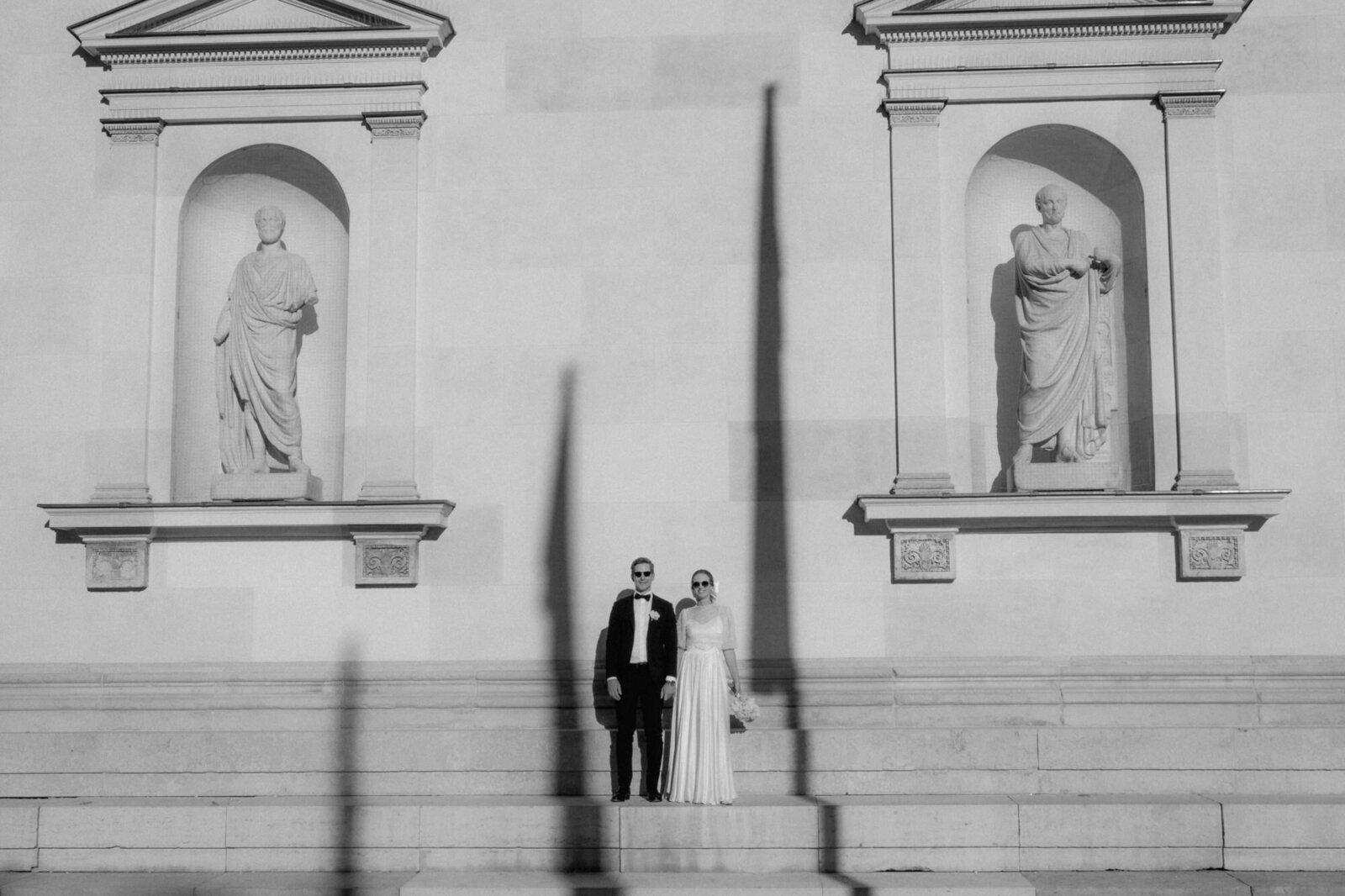 Wedding couple with sunglasses standing on stairs in front of a historical building.