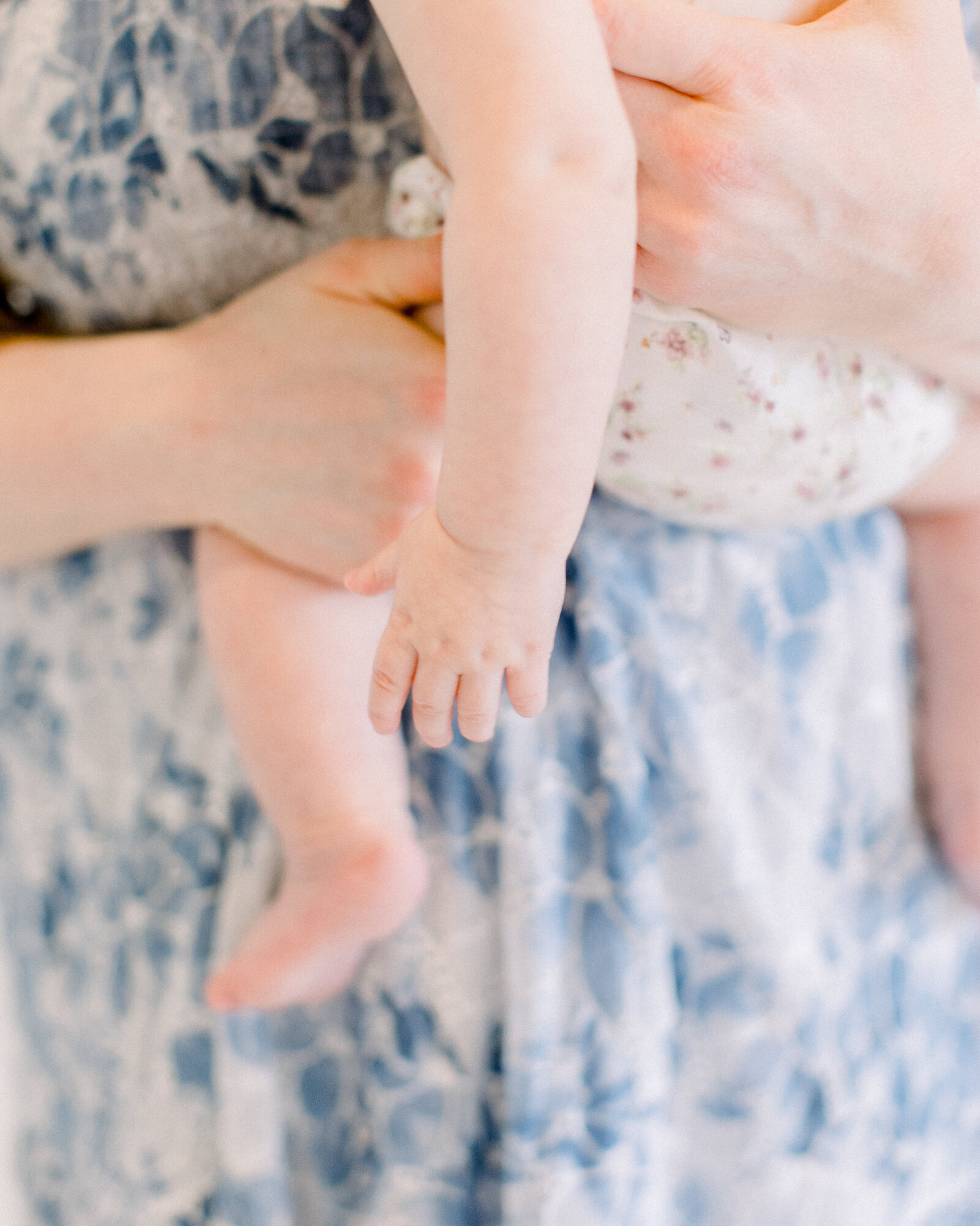 Closeup detail of mom's hands in blue floral gown, holding her baby on her hip in floral bloomers by NH newborn photographer Fieldstone Studio.