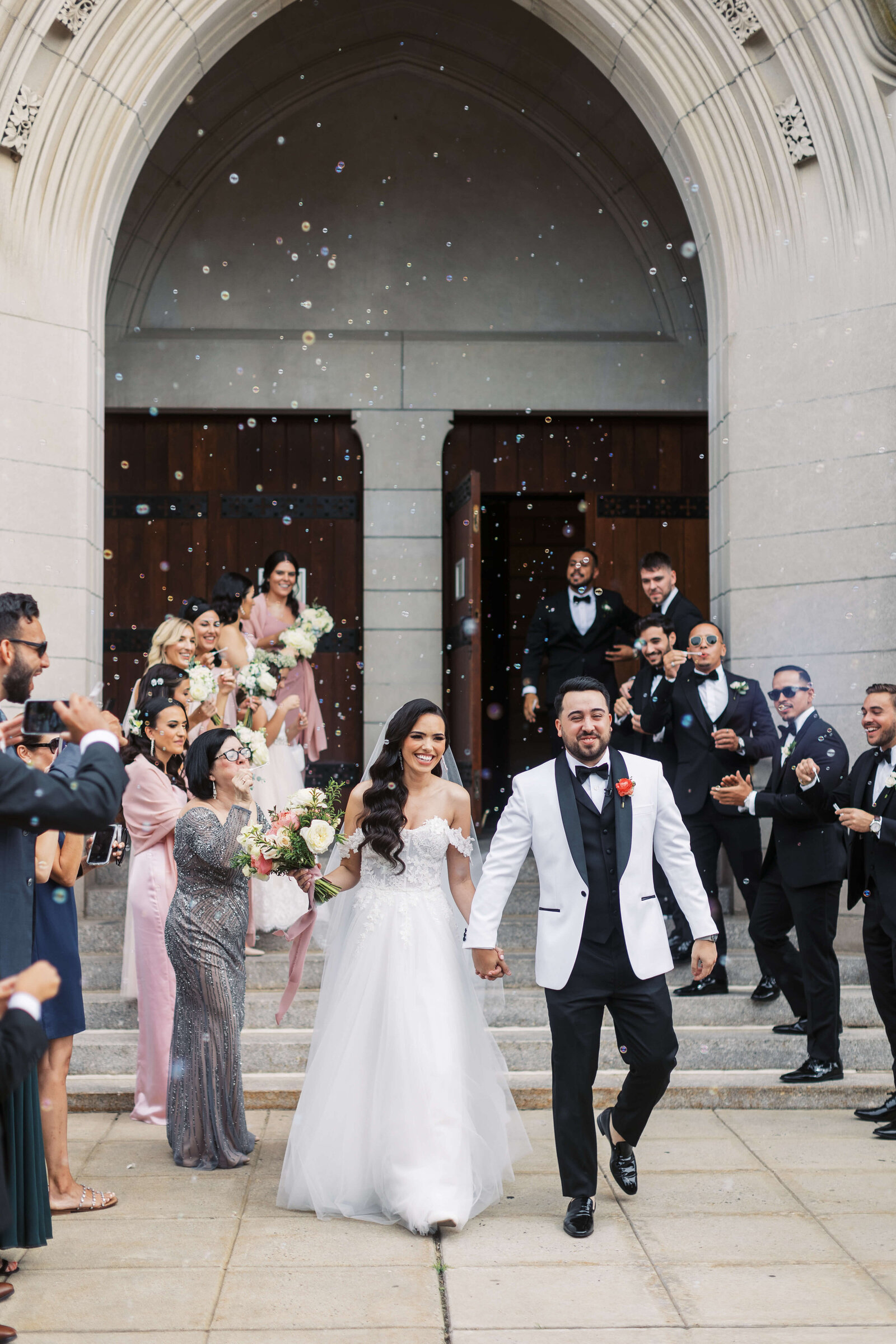 Husband and wife exit the church as their family and friends blow bubbles.