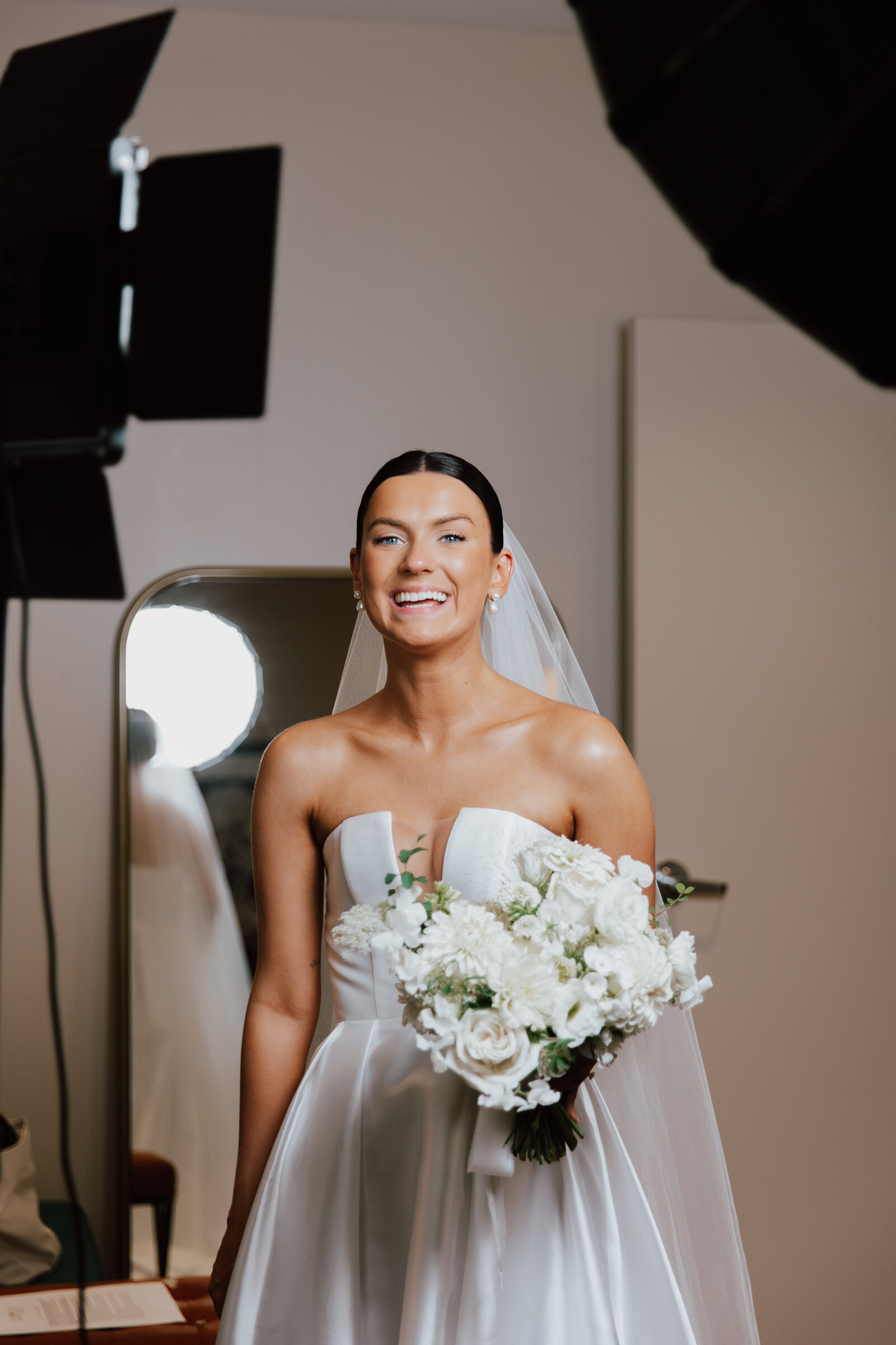Bride smiling in strapless gown, wearing a soft, textured hairstyle with a floral headband styled by Promise Artistry.