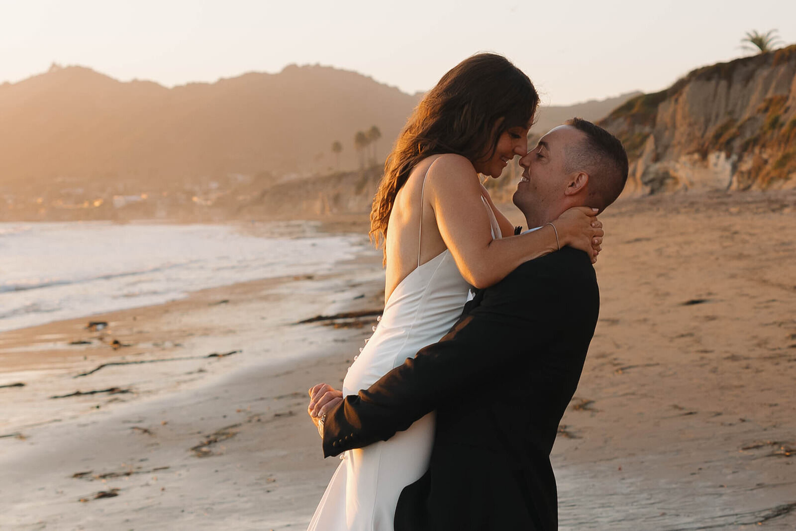 Bride and groom embracing on a California beach at sunset