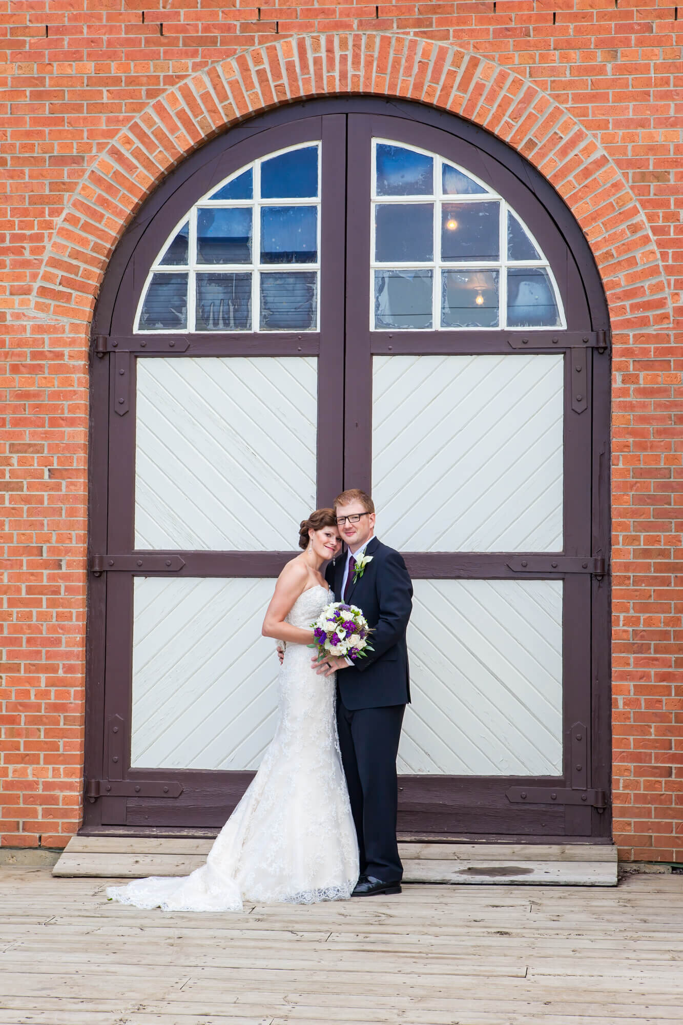 Bride and Groom posed in front of rustic doors  Fort Edmonton Park Wedding