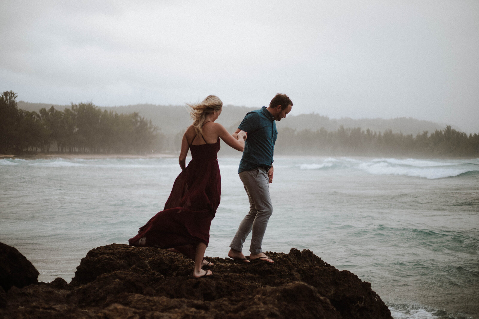 couple-walks-on-rocks-ocean-and-fog-in-background