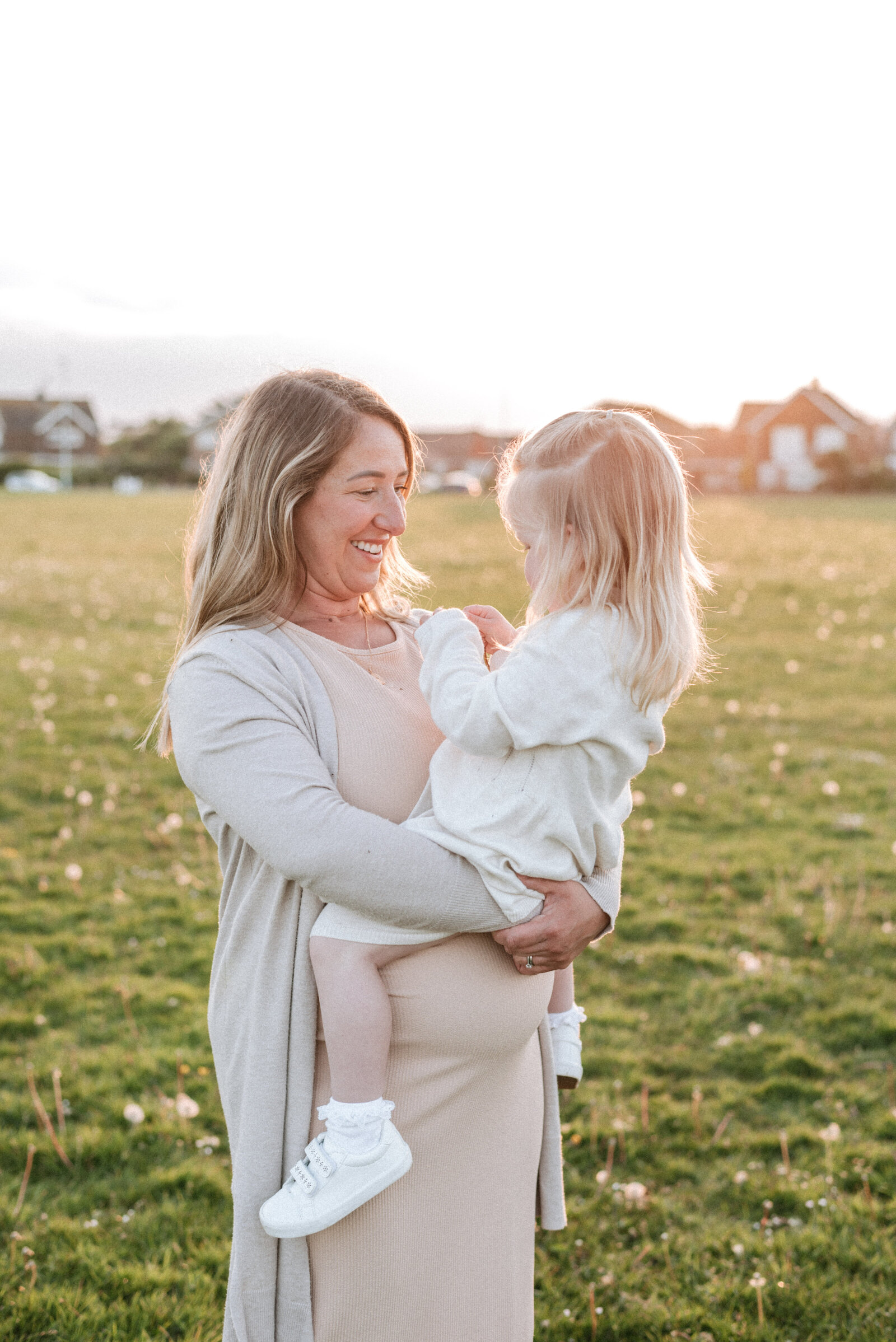Pregnant mum holding her daughter smiling at a sunset family photoshoot in Billingshurst West Sussex
