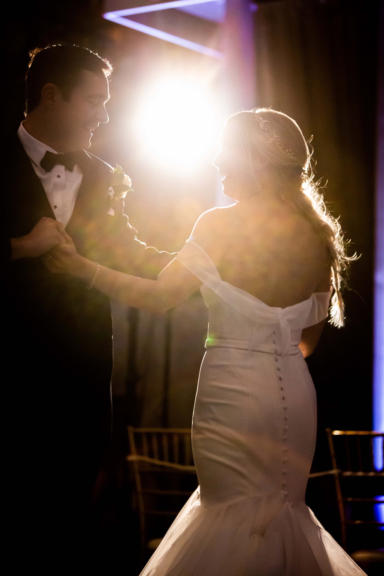 This mesmerizing photograph captures the unforgettable first dance of a newlywed couple, enveloped in a soft spotlight haze that adds a dreamlike quality to their special moment. The intimate ambiance is highlighted by the subtle play of light and shadows, creating a romantic scene that feels straight out of a fairy tale. Perfect for couples looking for wedding inspiration, this image not only portrays the love and connection between the couple but also the magical atmosphere of their wedding reception. A must-share for bridal websites and social media enthusiasts, it epitomizes the quintessence of wedding elegance and charm.