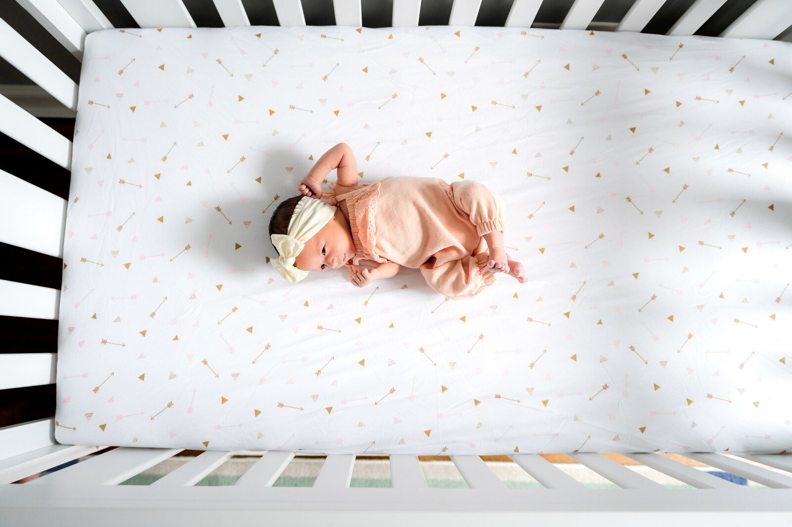 newborn baby in a pink onsie laying in the crib