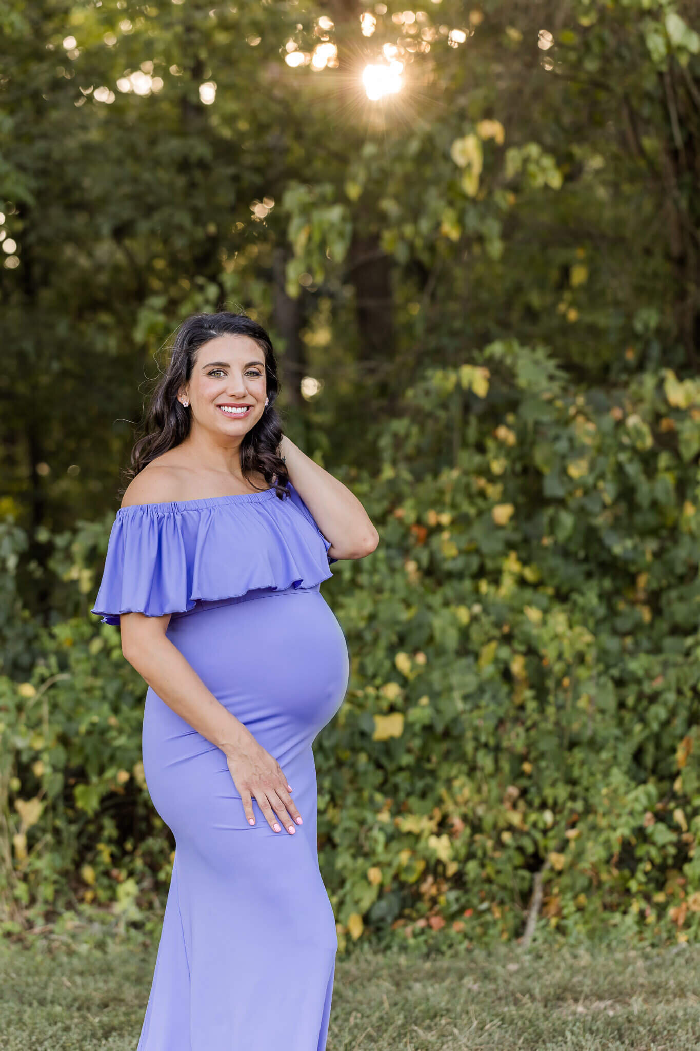 A mom-to-be wearing a purple gown posing in a park in Manassas, Virginia.