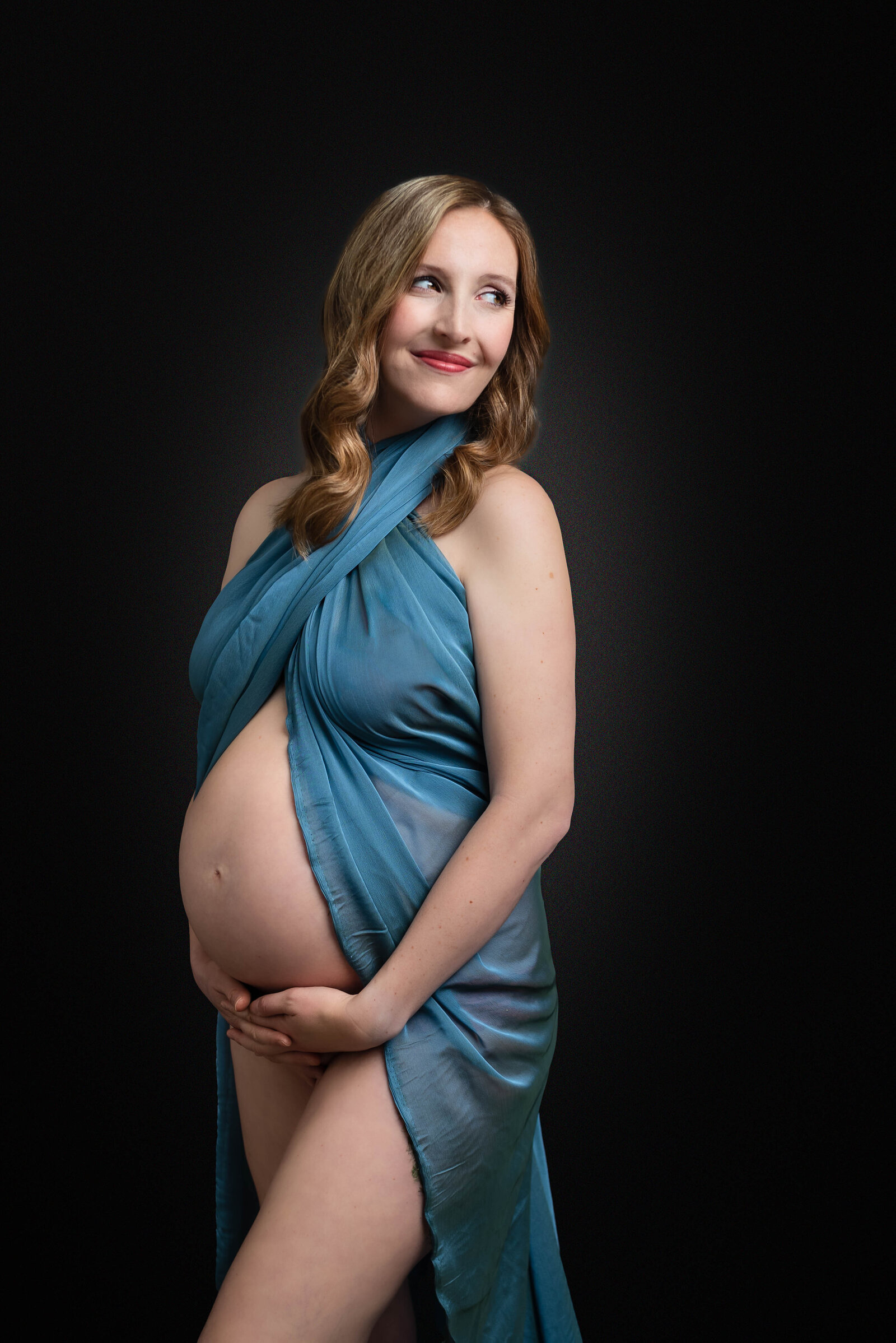 A pregnant woman draped in a blue fabric with her stomach exposed for her maternity photos in Huntsville Alabama