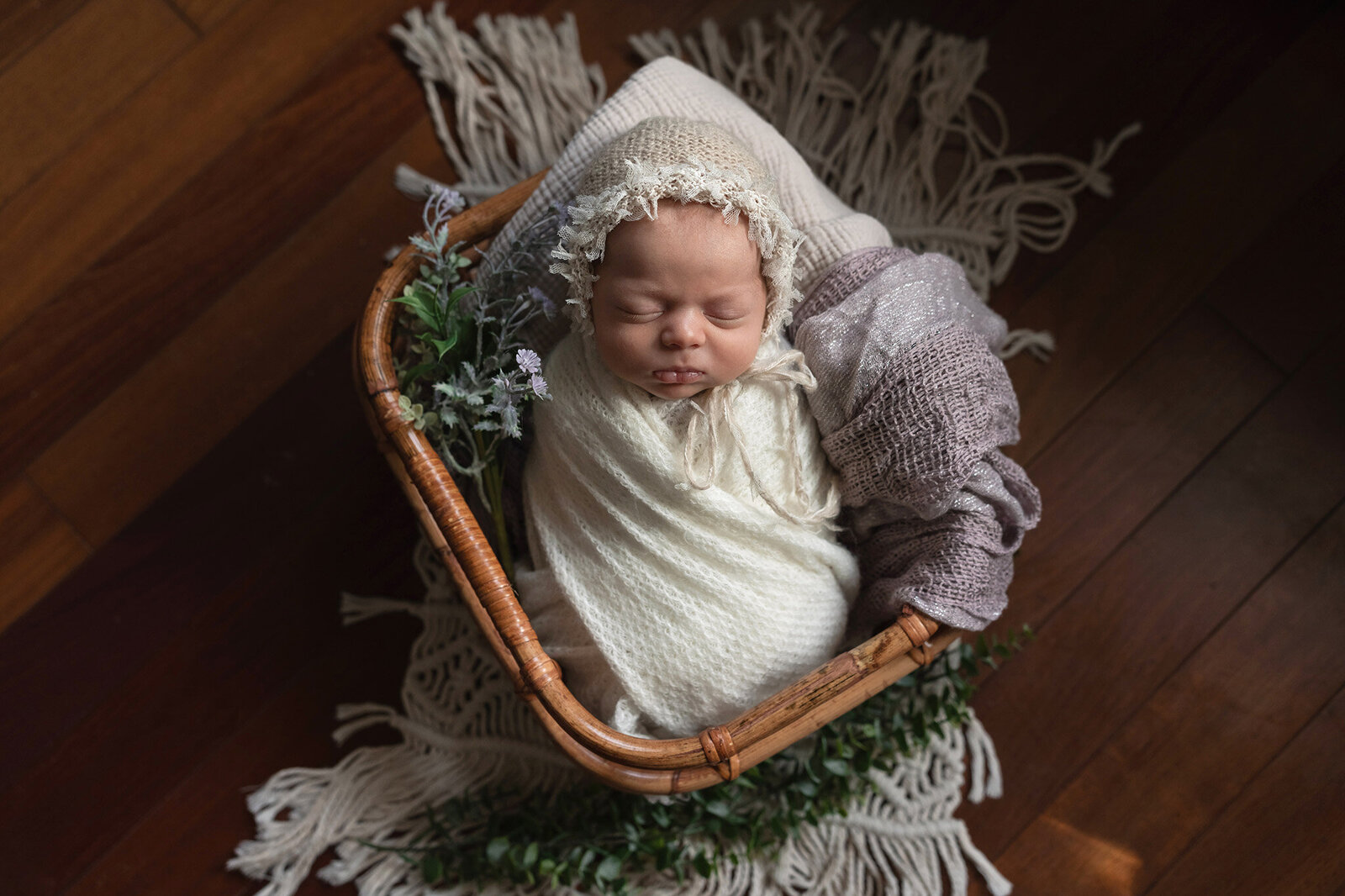 Posed newborn photo of baby girl in a basket with a bonnet