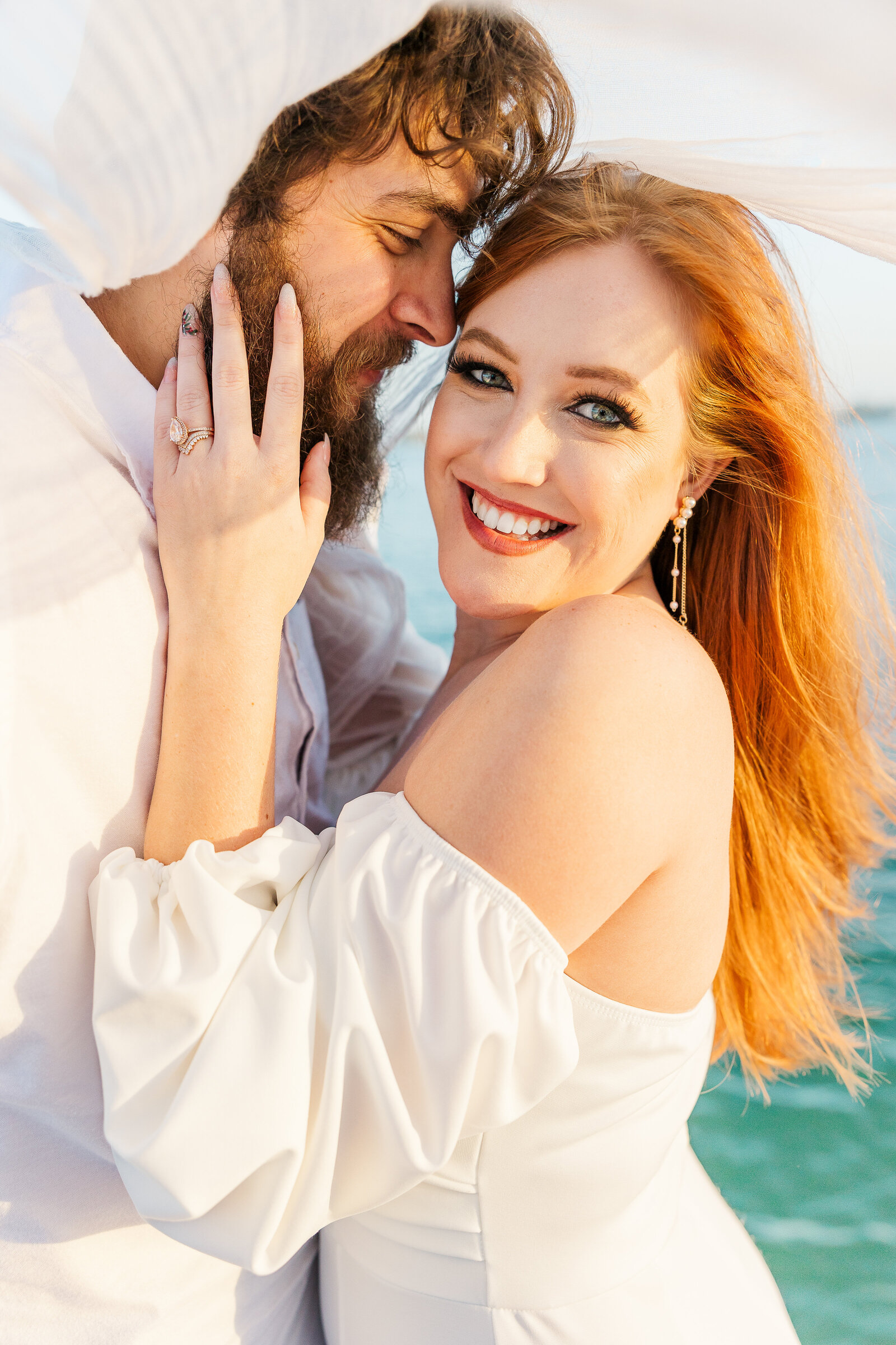 A newly married couple embraces on a sailboat as the bride smiles at the camera