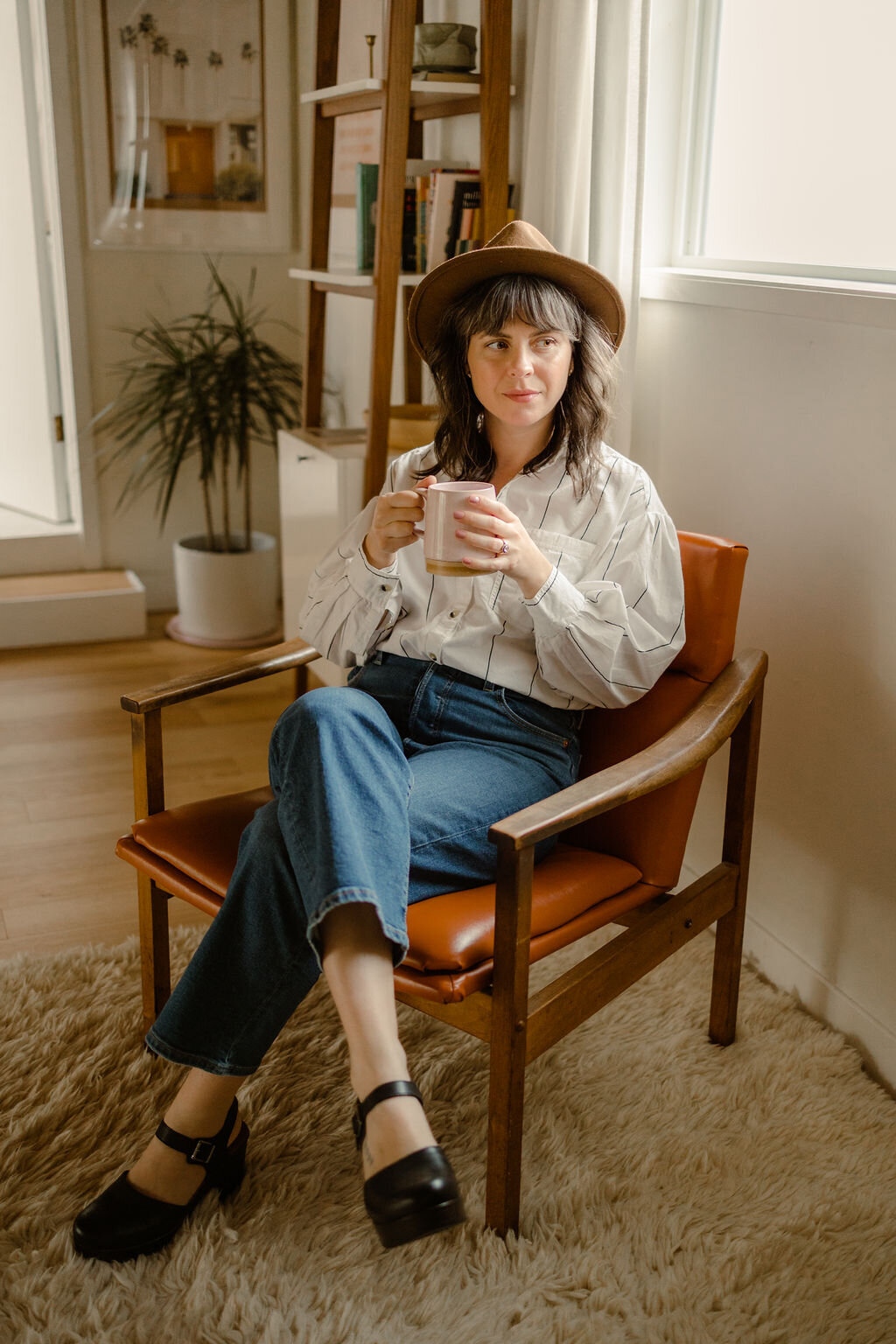 Web designer Carrie Bondioli sits in a chair and holds a cup of coffee.