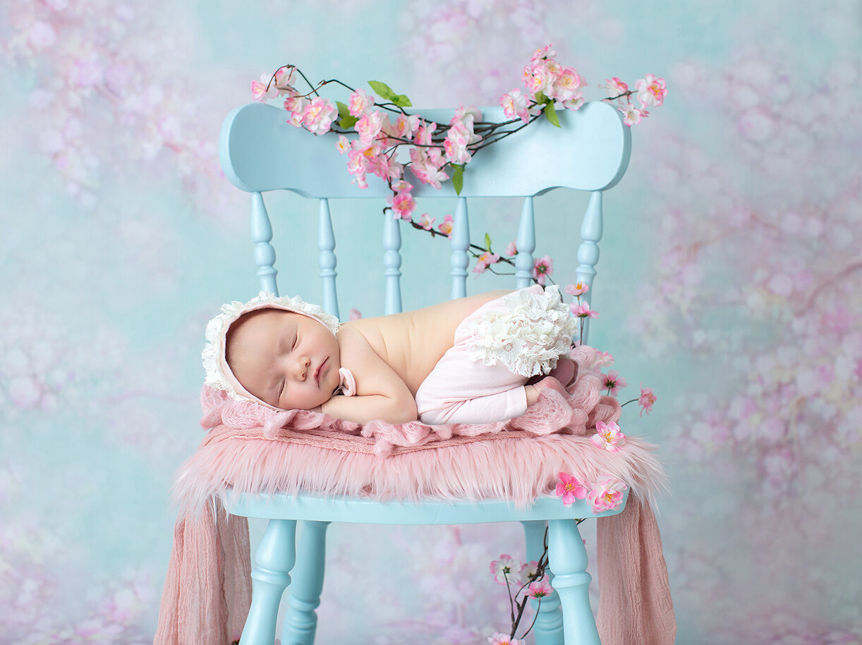 Newborn on blue chair with pink flowers.