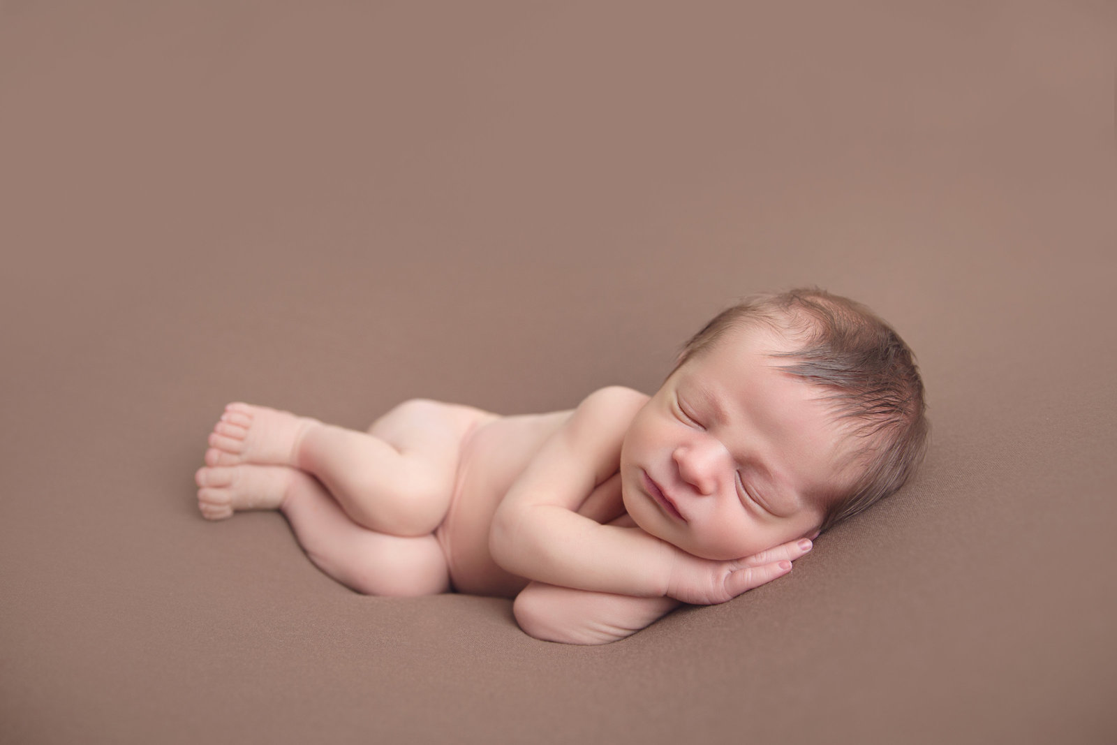 sleeping newborn baby posed on brown fabric in side laying pose