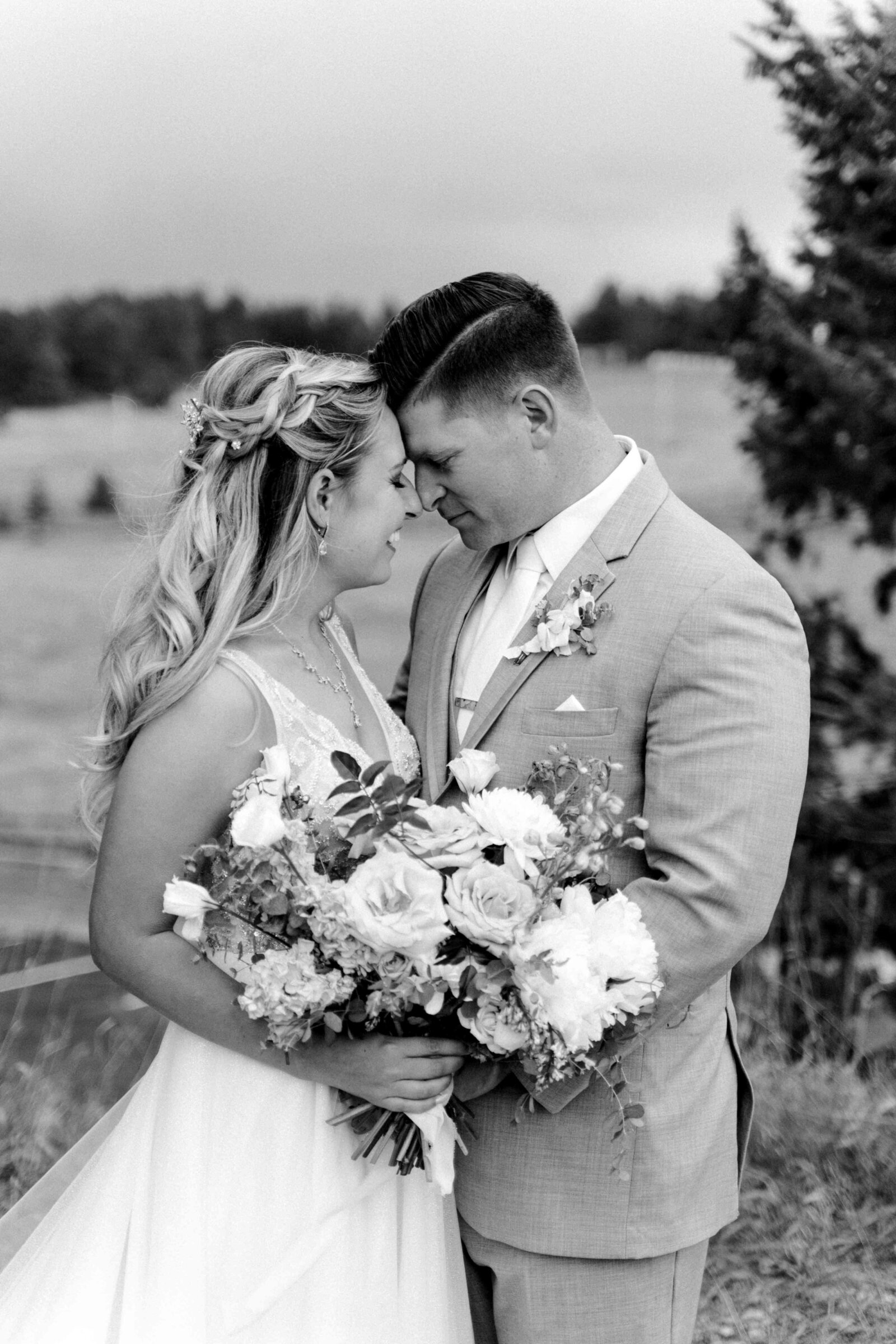 Black and white photo of bride and groom facing each other about to kiss while holding floral bouquet