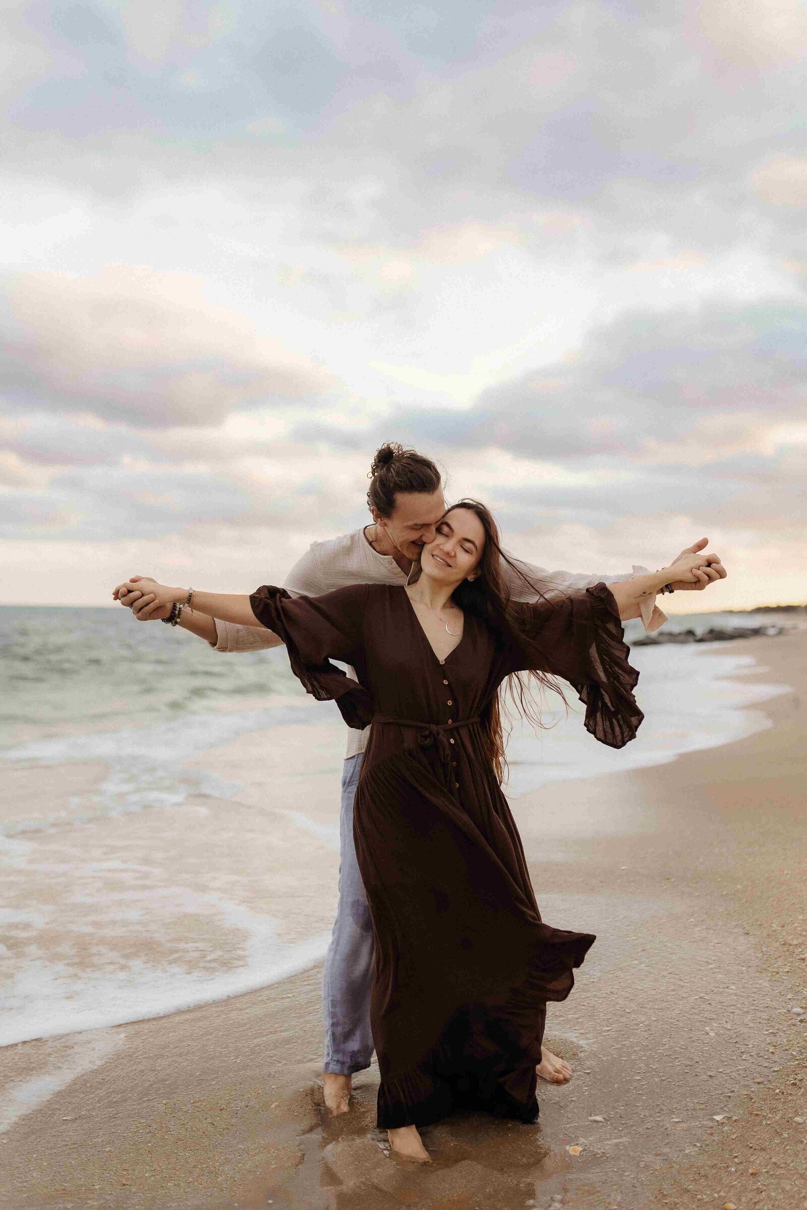 Miami beach photographer captures romantic pose of a couple with outstretched arms on the sand, with ocean waves