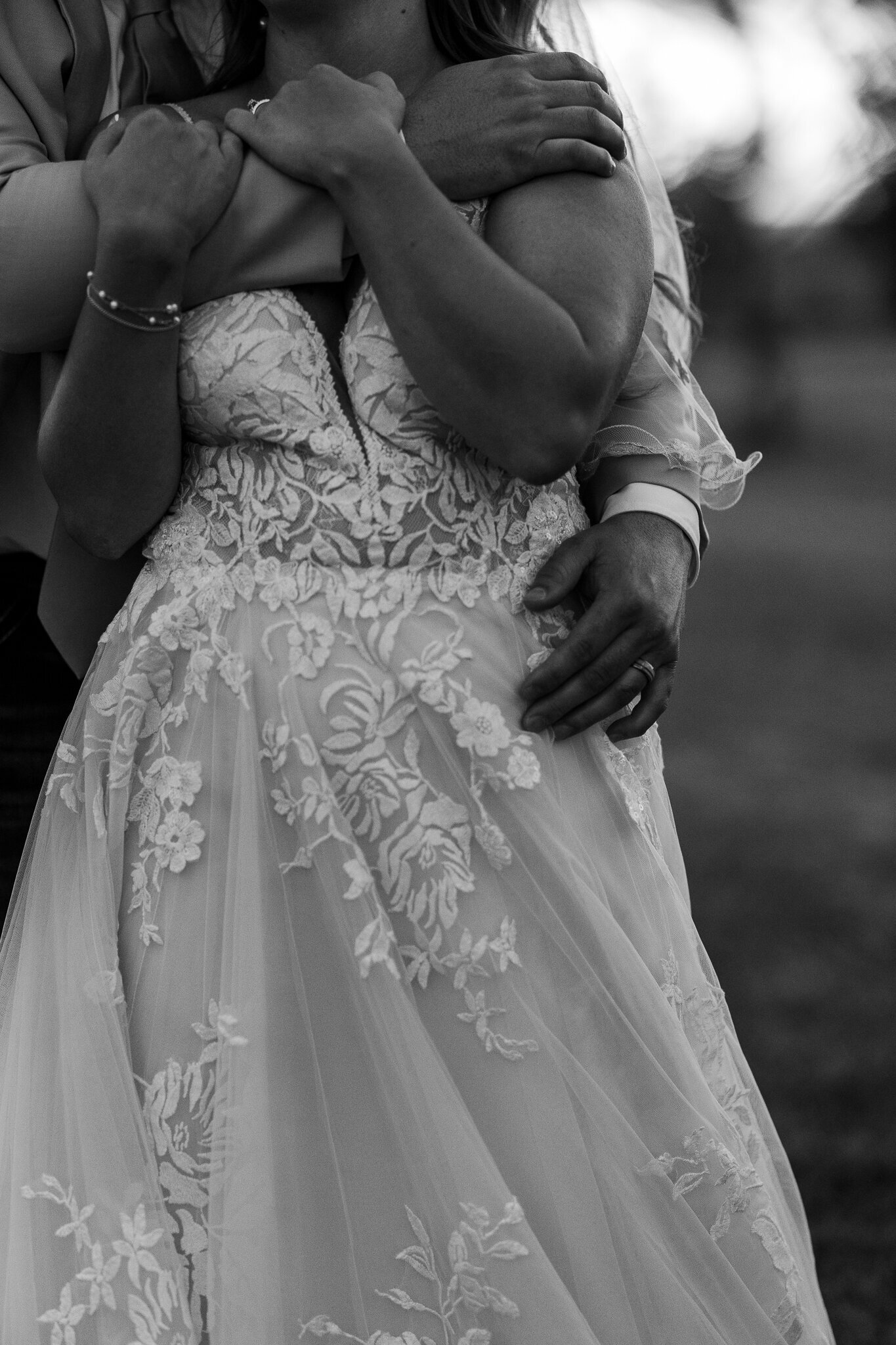 Black and white close-up of the groom’s hand resting on the bride’s lace dress at their Loma, Colorado wedding