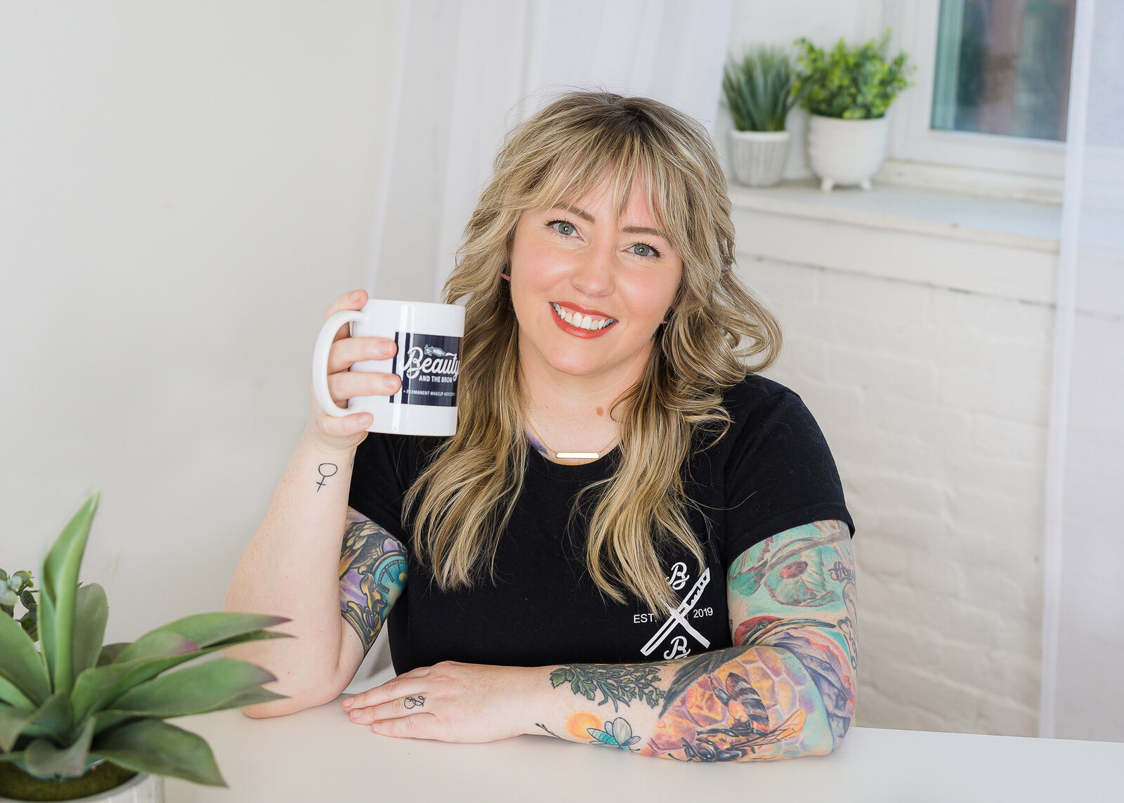 Woman sitting at a desk surrounded by white walls holding a cup of coffee