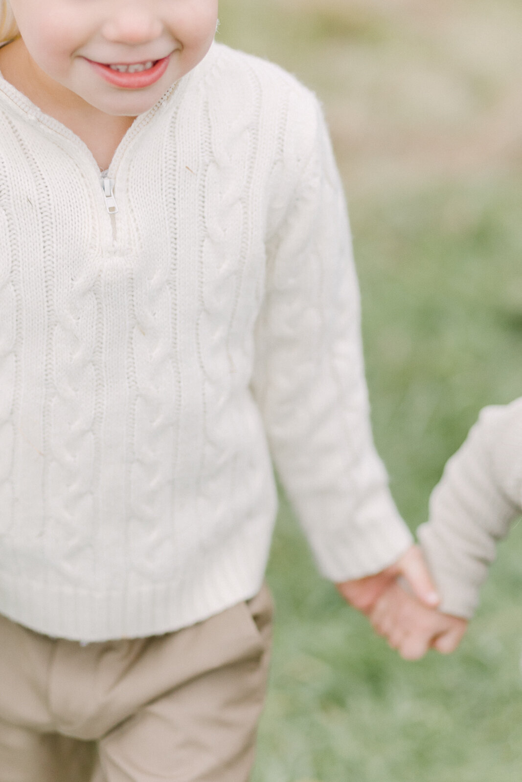 A close up image focusing on a young boy holding his little sister's hand while walking in a field