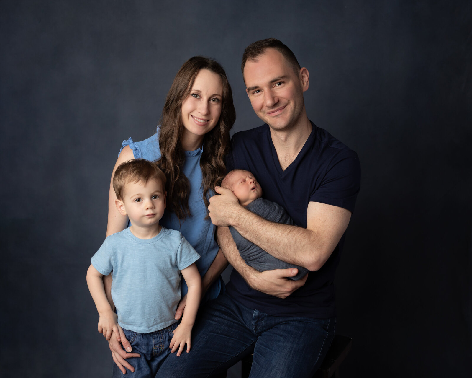 mom and dad and brother holding newborn baby boy wrapped in blue for newborn studio portraits