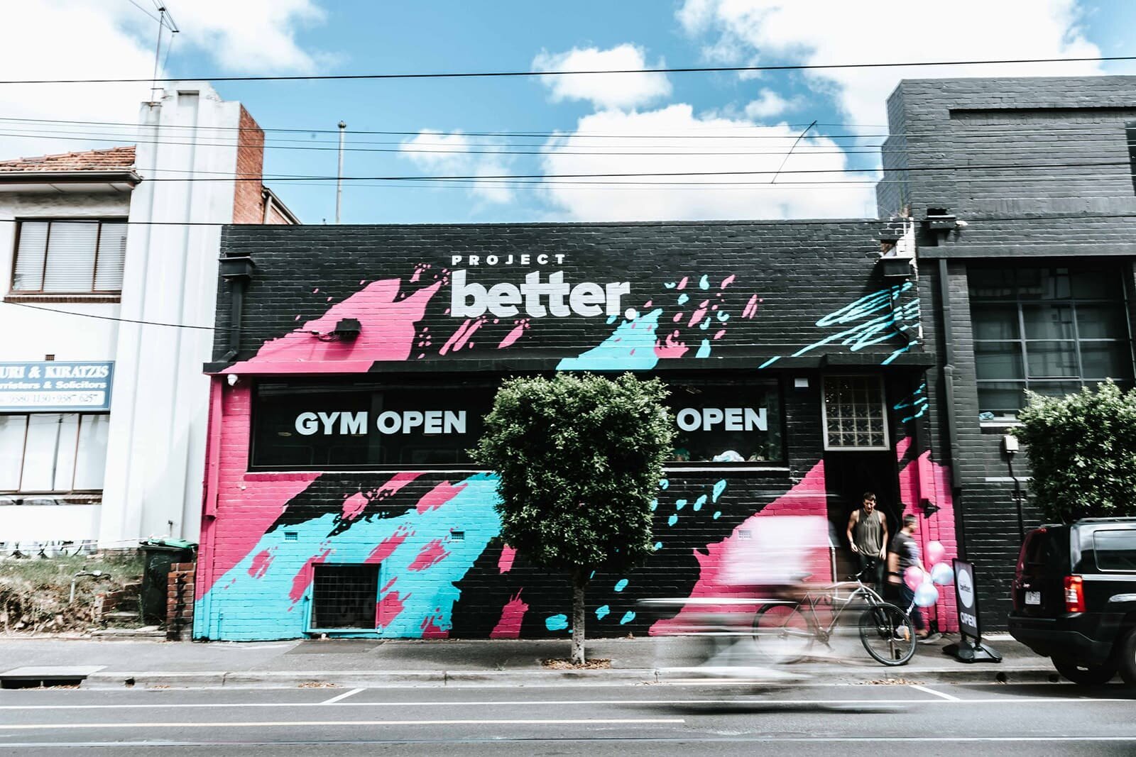 "Front exterior of a Brunswick gym featuring vibrant pink and blue graffiti and a large 'Gym Open' sign."