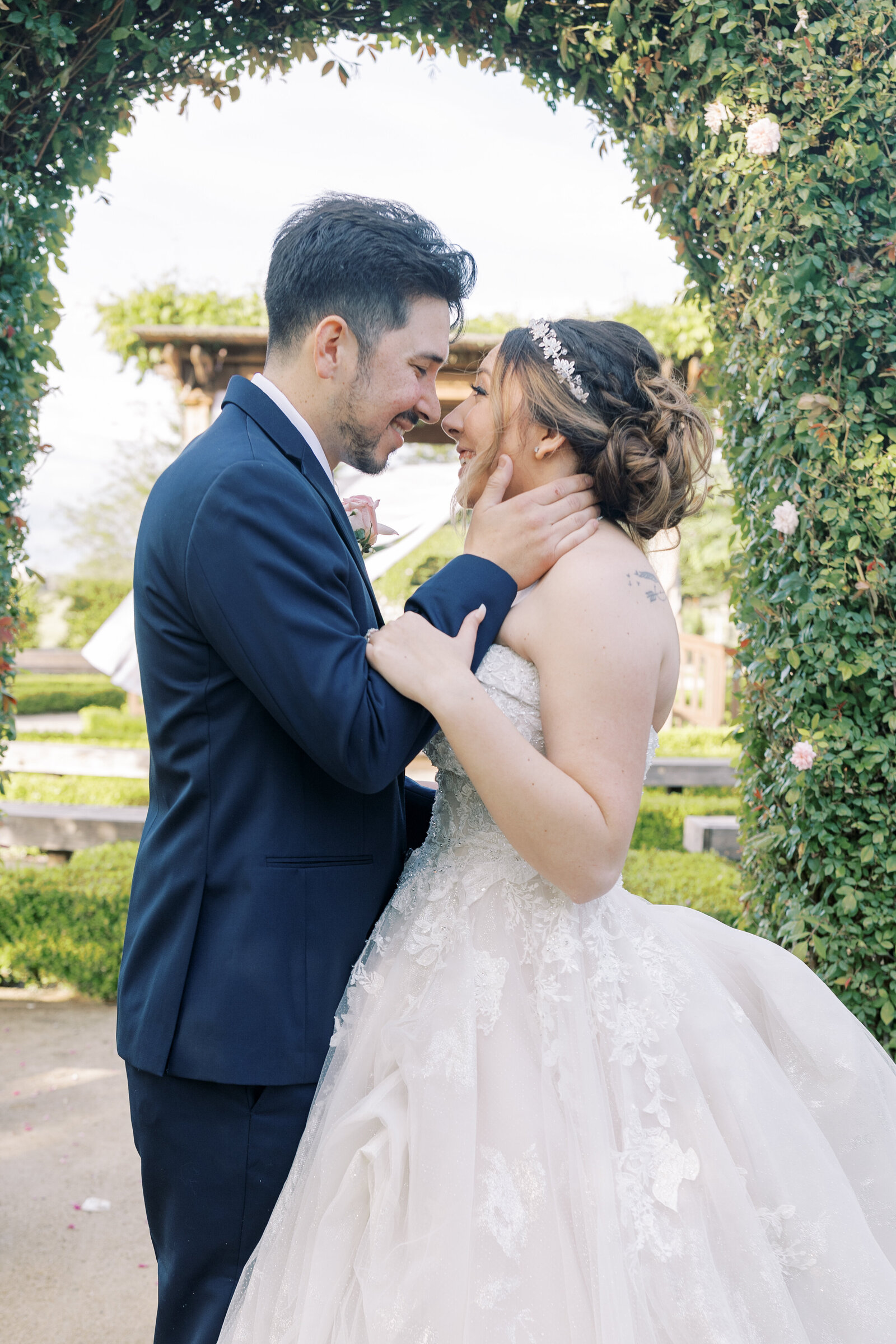 sacramento wedding photographer captures outdoor wedding with man and woman embracing in a courtyard next to a lush wall of hedges while the groom holds the womans face