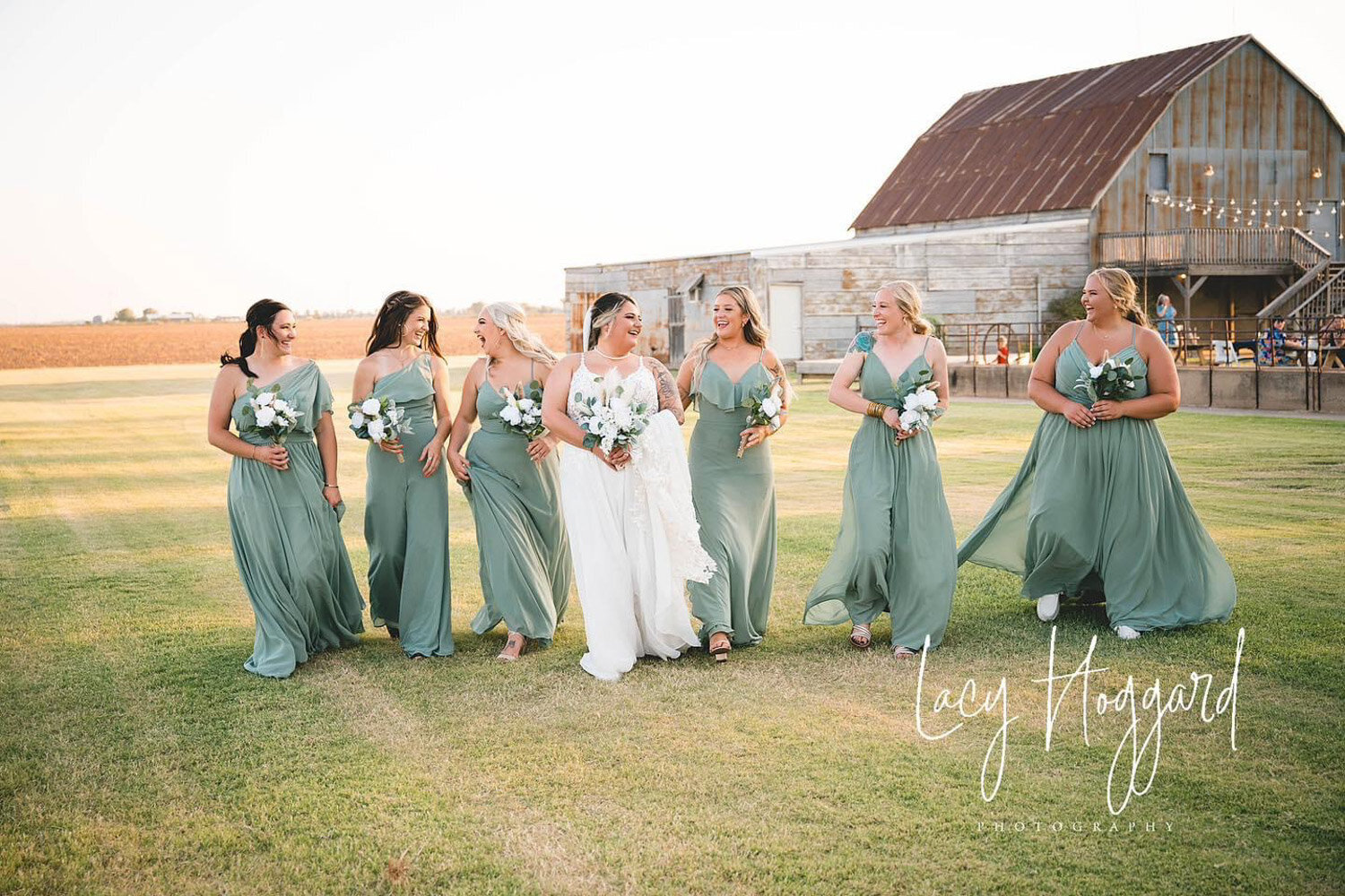 Bride walking with her bridesmaids in sage green dresses outside a rustic barn