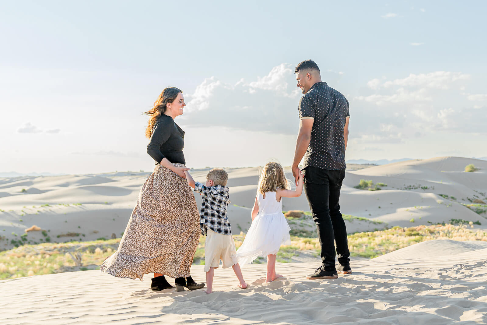 Utah family photography of family of four looking at each other while standing on a sand dune at Little Sahara, Nephi.
