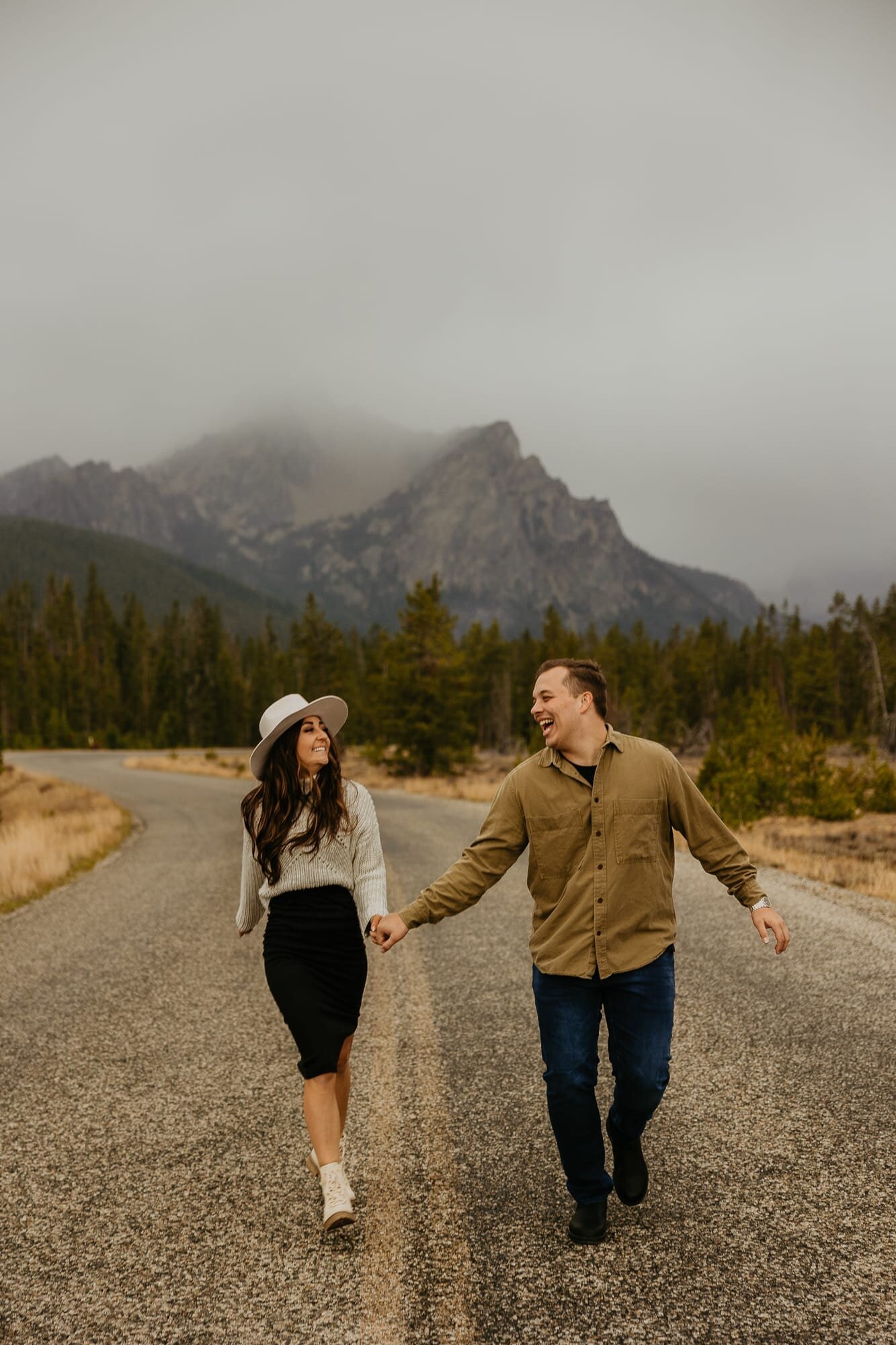 A couple running on the road during their engagement photo session in Stanley, Idaho