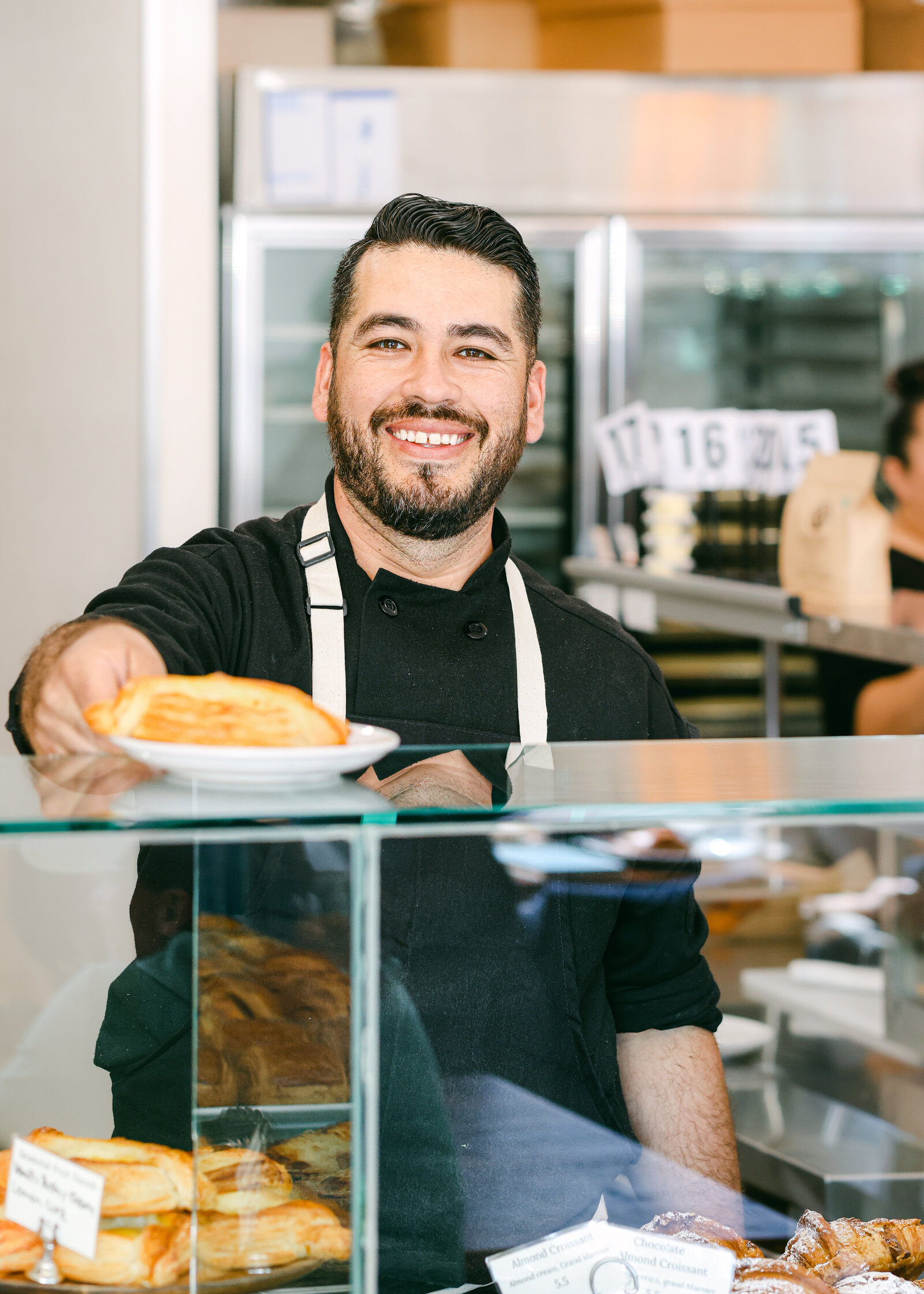 baker serving croissant pastry at bakery friendly smiling over counter