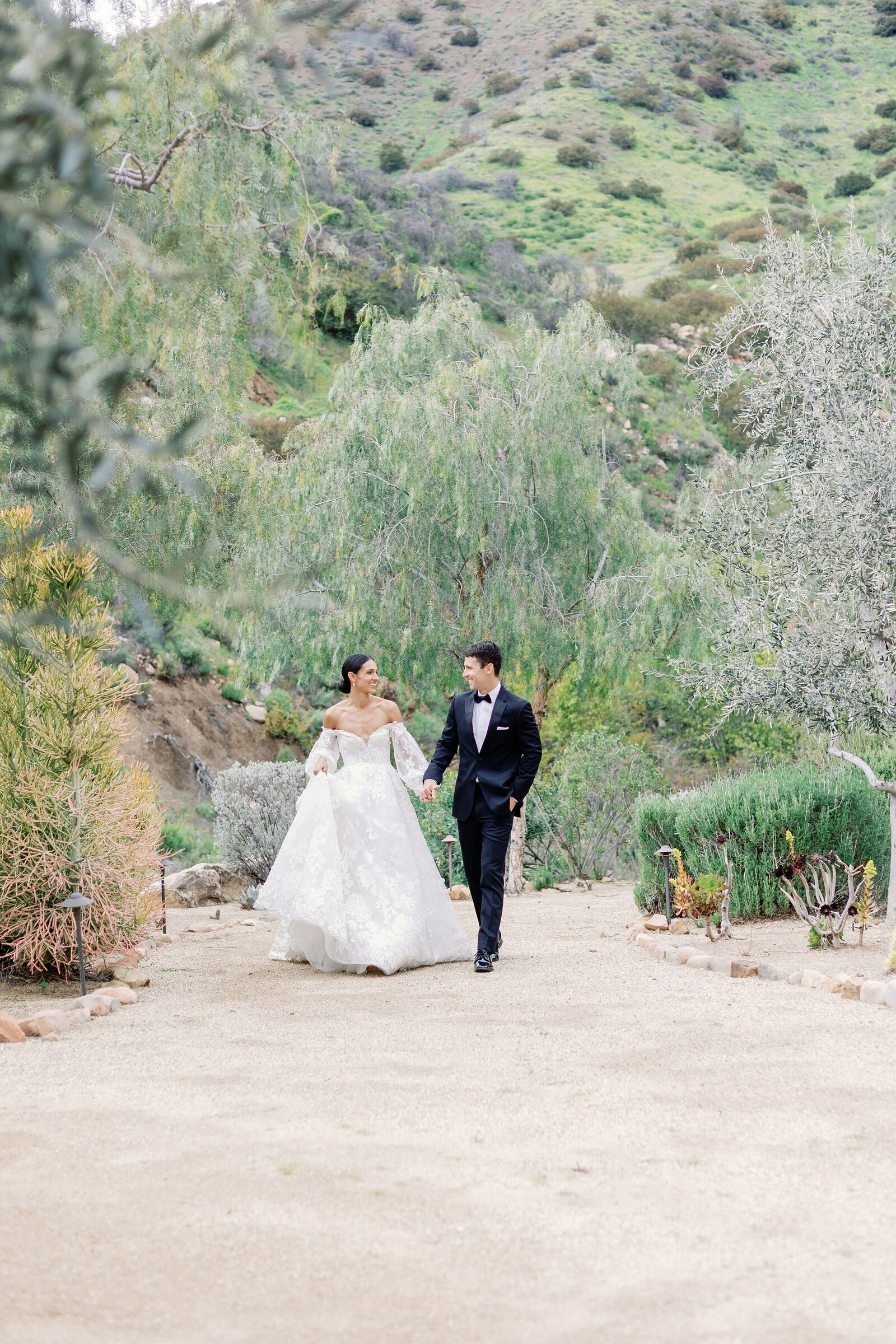 wedding photographer bay area documents wedding pictures of bride and groom holding hands and walking down a dirt path together at their California wedding venue