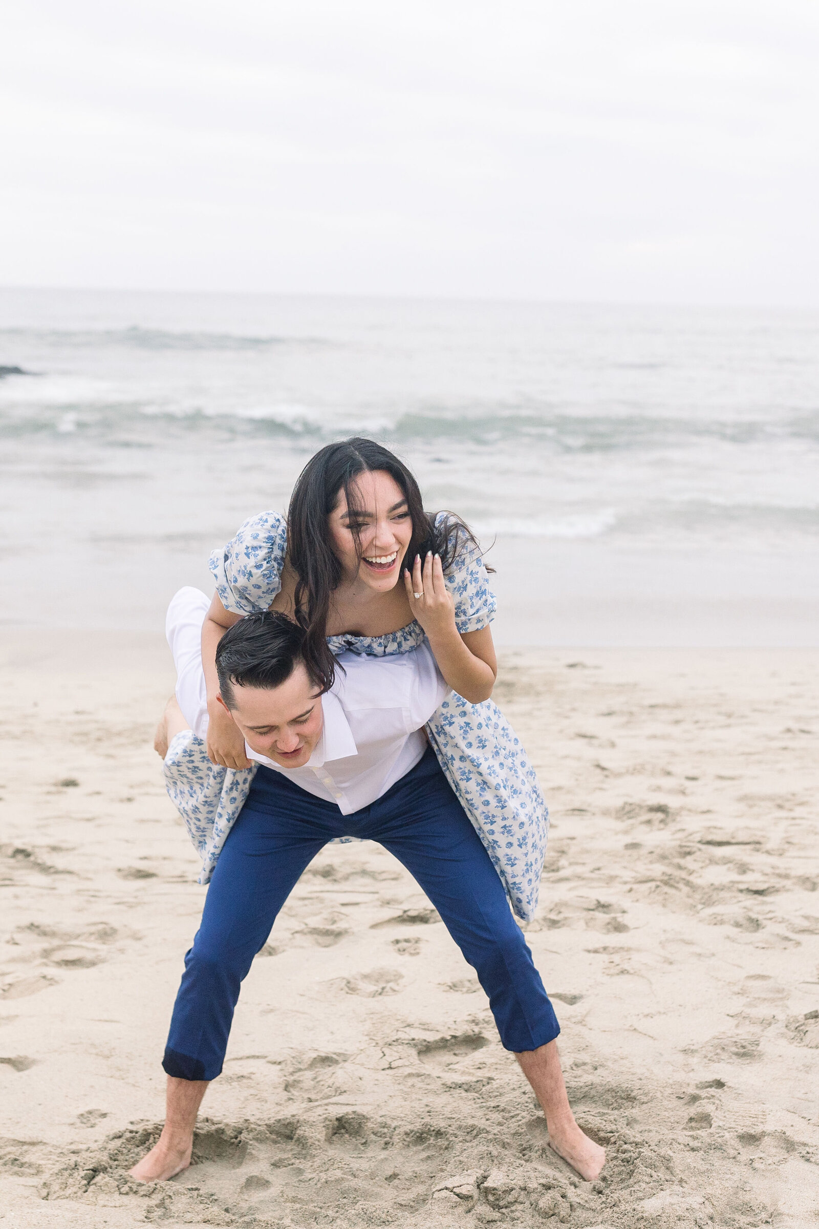 wedding photographer bay area captures proposal pictures with woman on mans back for a piggy back ride holding her ring in the air for a beach engagement photos