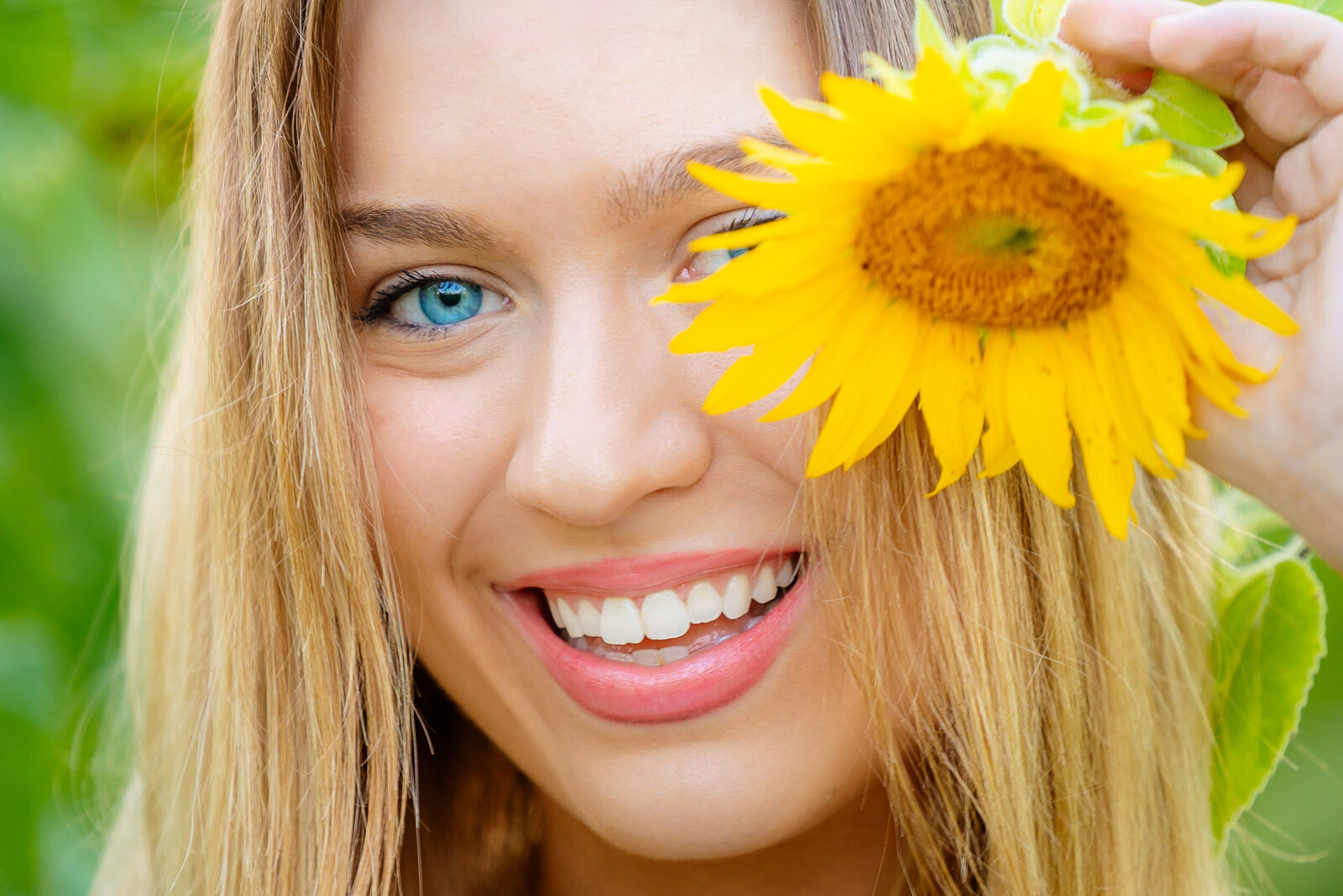 extreme close up of senior with a huge sunflower over one eye and smiling in the sunflower field in St. Louis MO