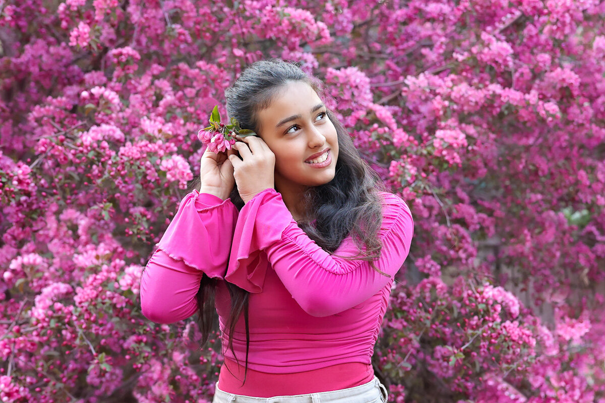 Girl with long hair is fixing a flower in crab apple photo session in Calgary by Yuliia Terziian Photography