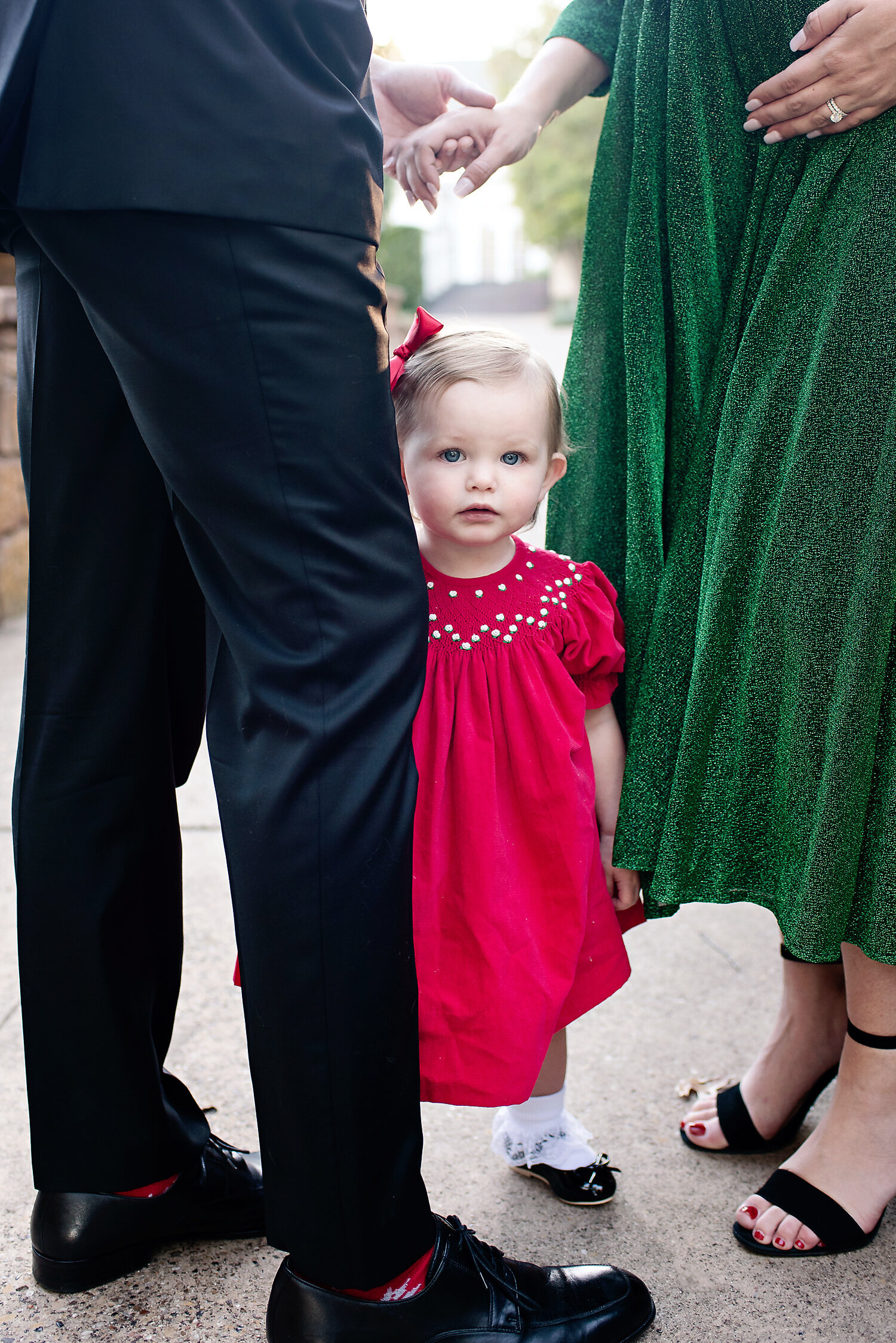 A young girl in a red dress standing between her parents and looking directly at the camera.