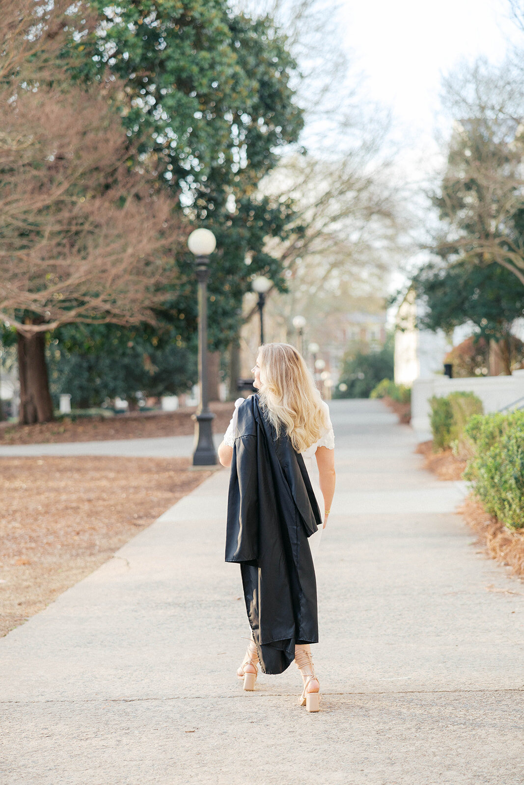 Girl walks and holds graduation gown over her shoulder and looks out to the lawn on UGA's campus