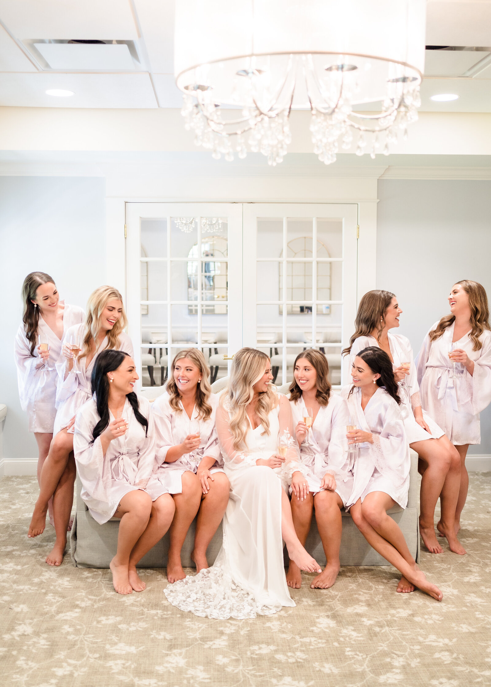 Bride and her bridesmaids sit on a couch and smile at each other in their getting ready robes