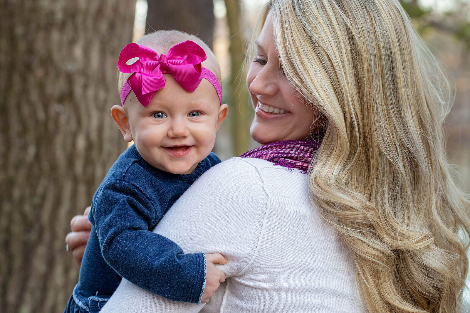 A mom holding her baby girl who is looking over her shoulder and smiling.