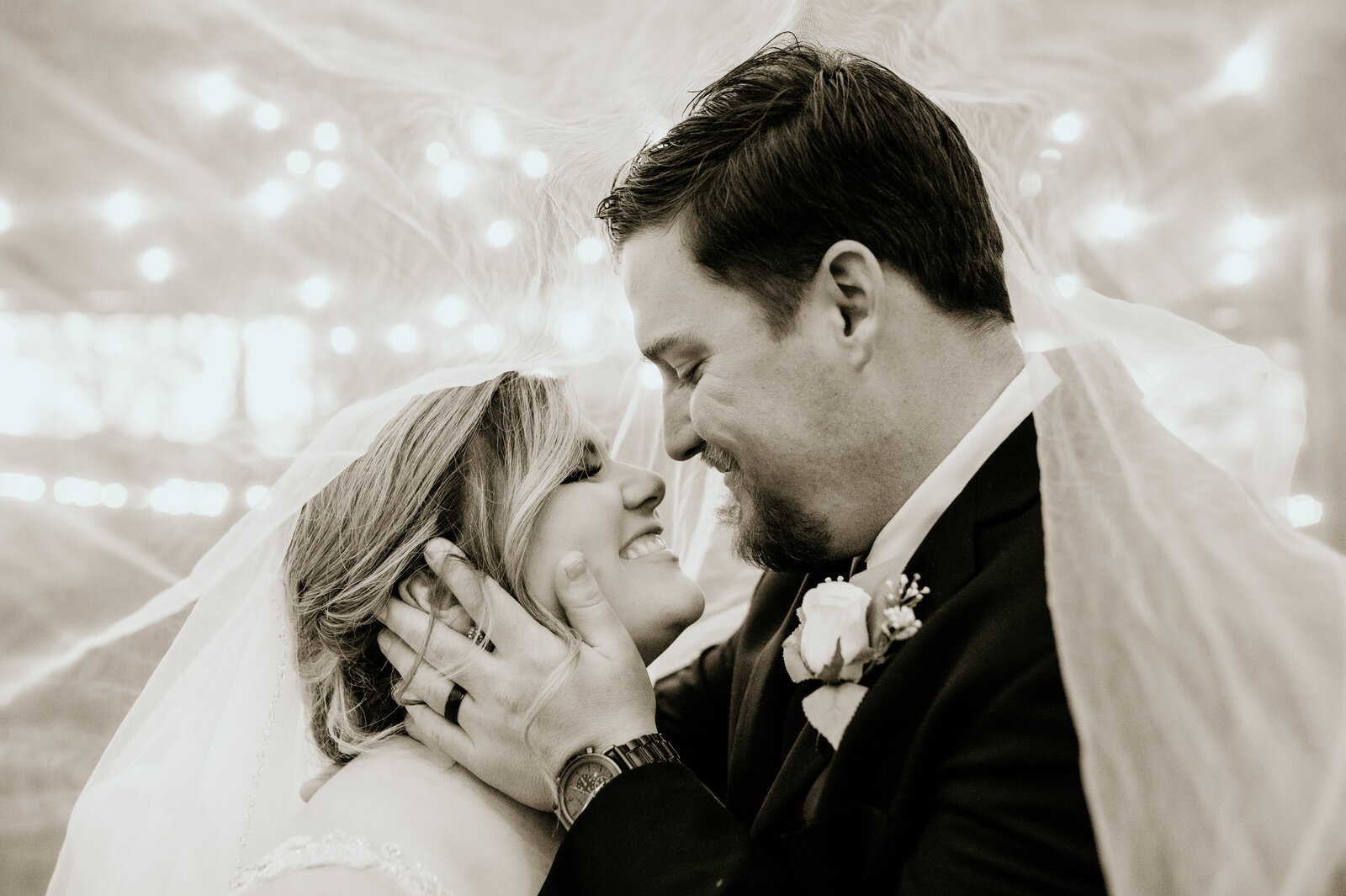 bride and groom smiling with each other under the brides veil while the groom holds her face romantically