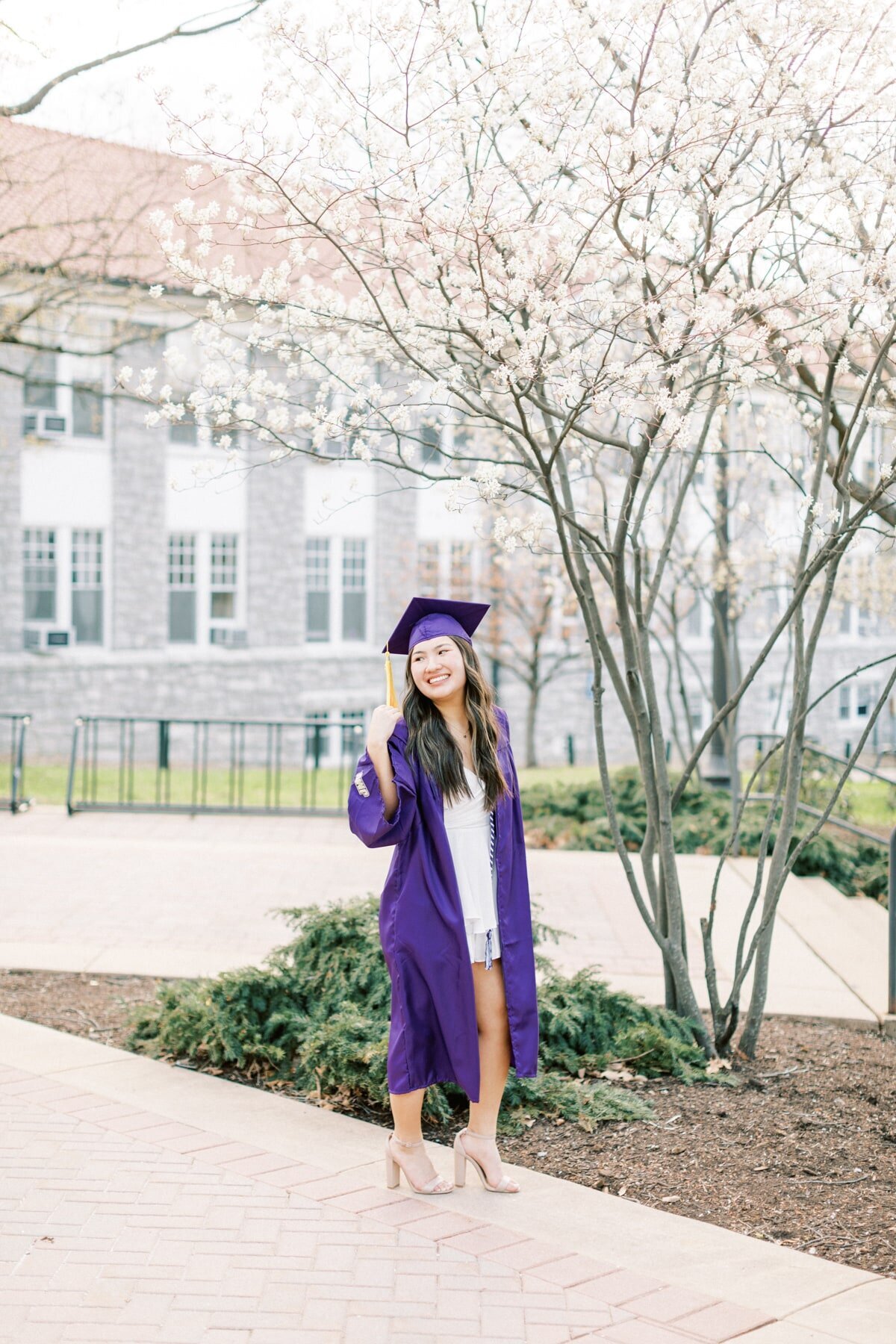 A JMU graduate loks over her shoulder smiling as she has her photos taken by Rachel Jordan Photography.