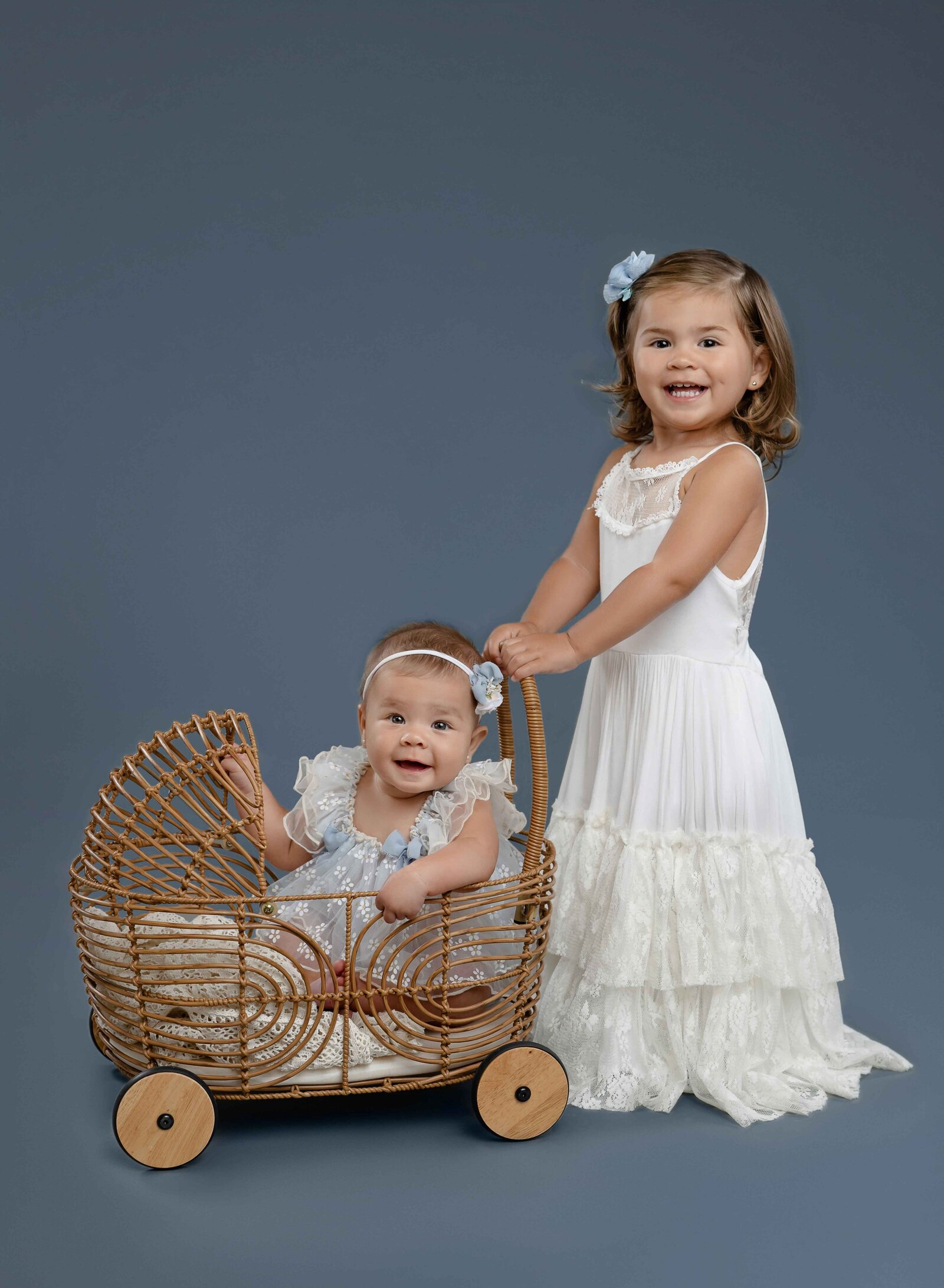 Big sister pushing 6 month old baby girl in bamboo carriage.
