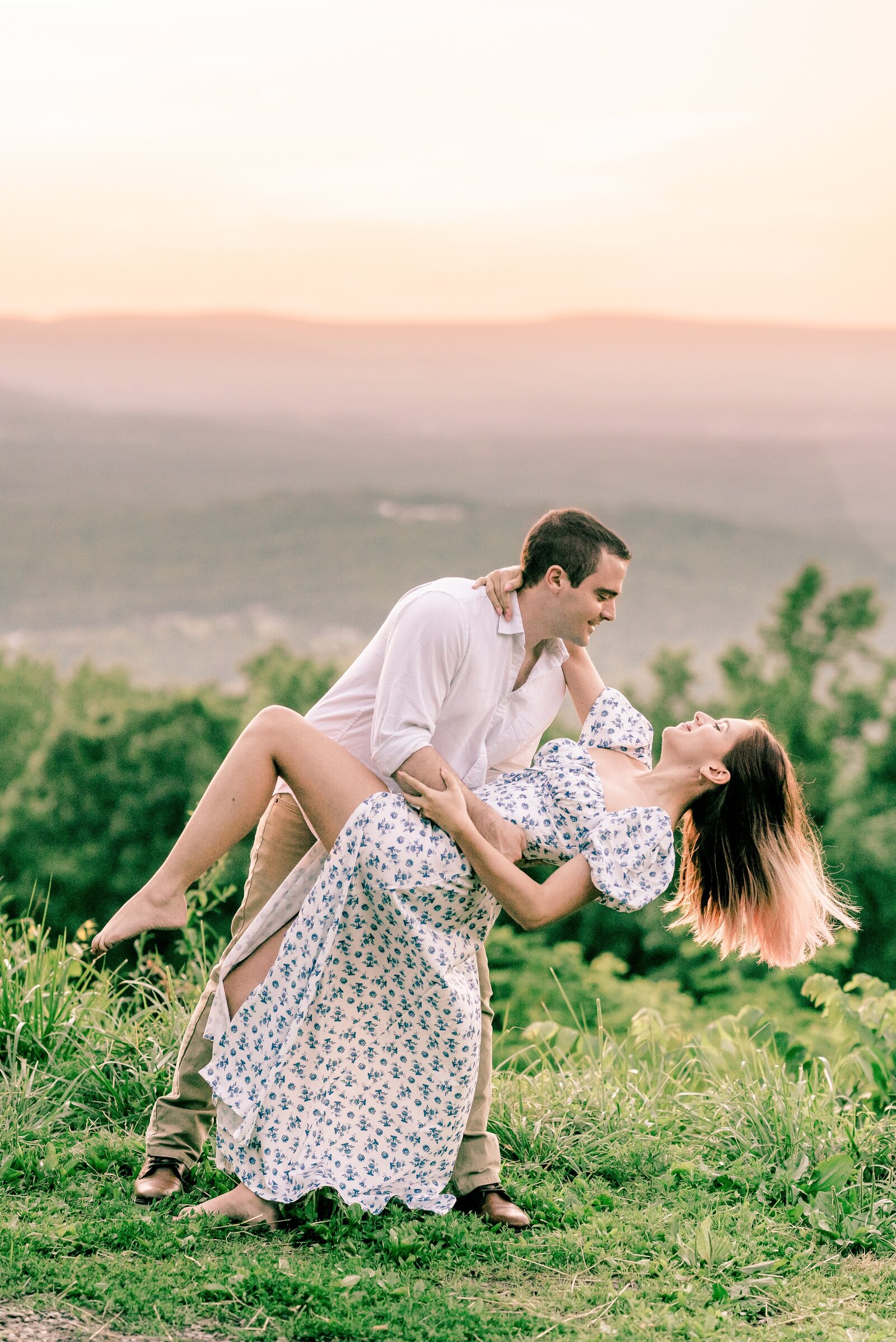 An engaged couple shares a dramatic dip on a mountain overlook during their engagement session at Shenandoah National Park in Northern Viginia