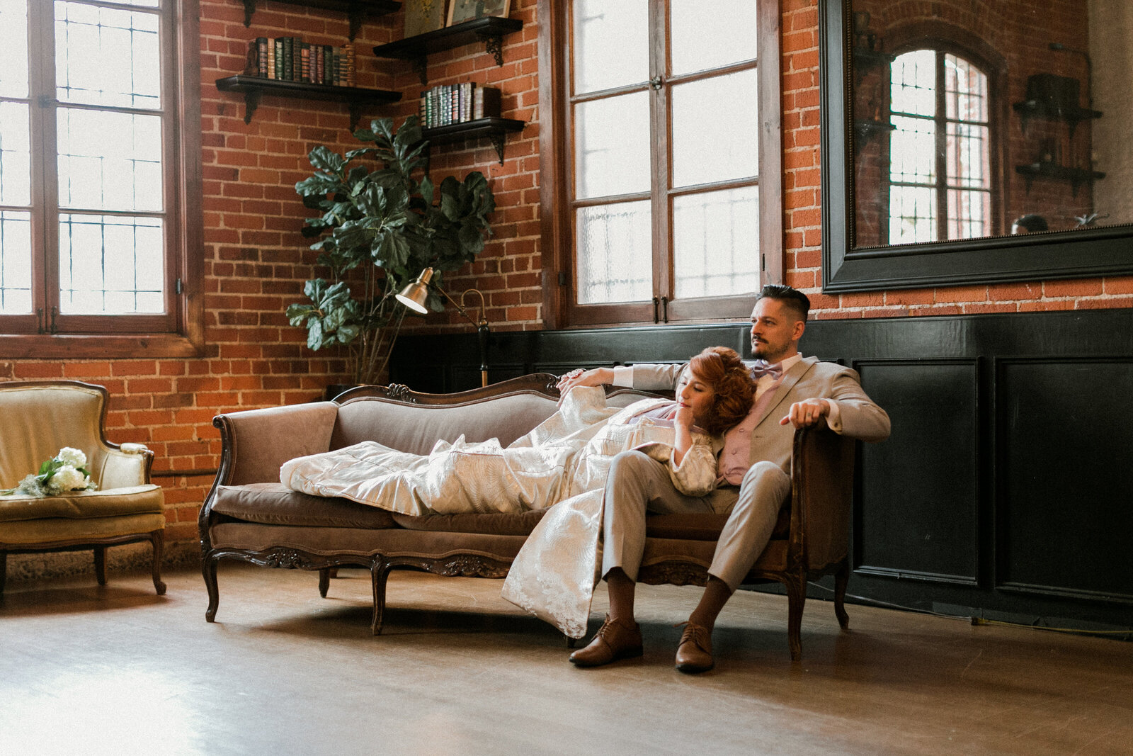 Bride in pale lavender and light gray shiromuku wedding kimono holding a white bouquet, seated with groom on vintage sofa at Carondelet House, Los Angeles California — elegant Japanese kimono rental photo | ラベンダーとグレーの白無垢でブーケを持つ花嫁と新郎がカロンデレットハウスのヴィンテージソファで撮影 ロサンゼルス カリフォルニア 着物レンタル